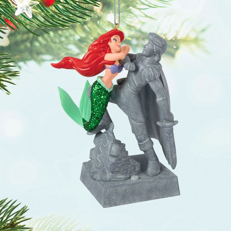 A Hallmark Disney Keepsake Ornament shows Ariel hugging Prince Eric’s statue, with festive lights like those in Disney park displays.