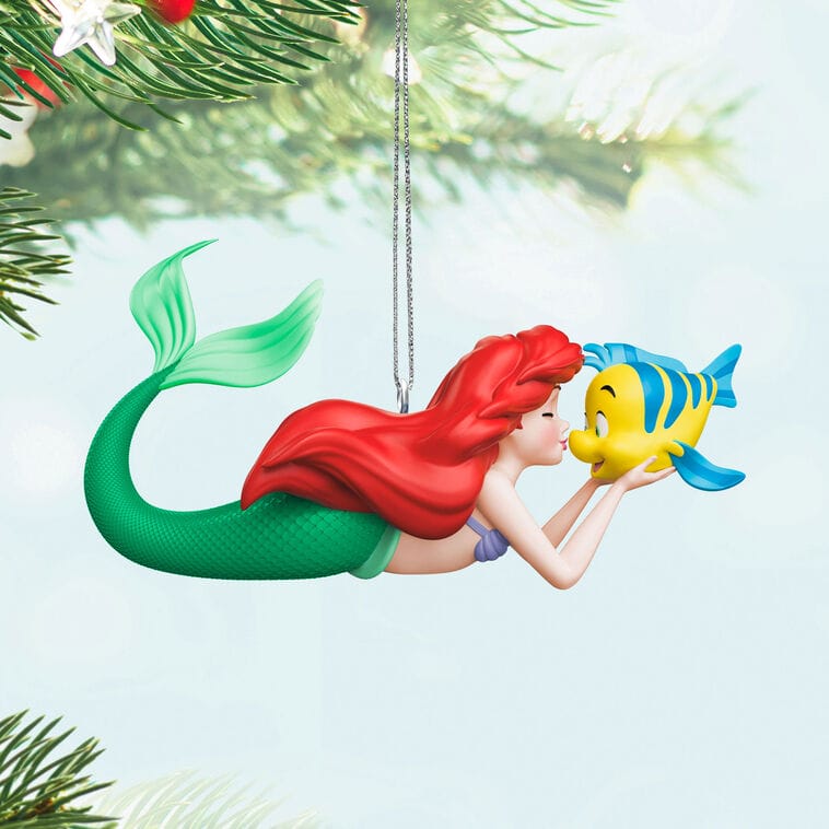 A Hallmark Disney Keepsake Ornament of Ariel and Flounder, like those found in Disney Parks shops, hangs from a tree branch.