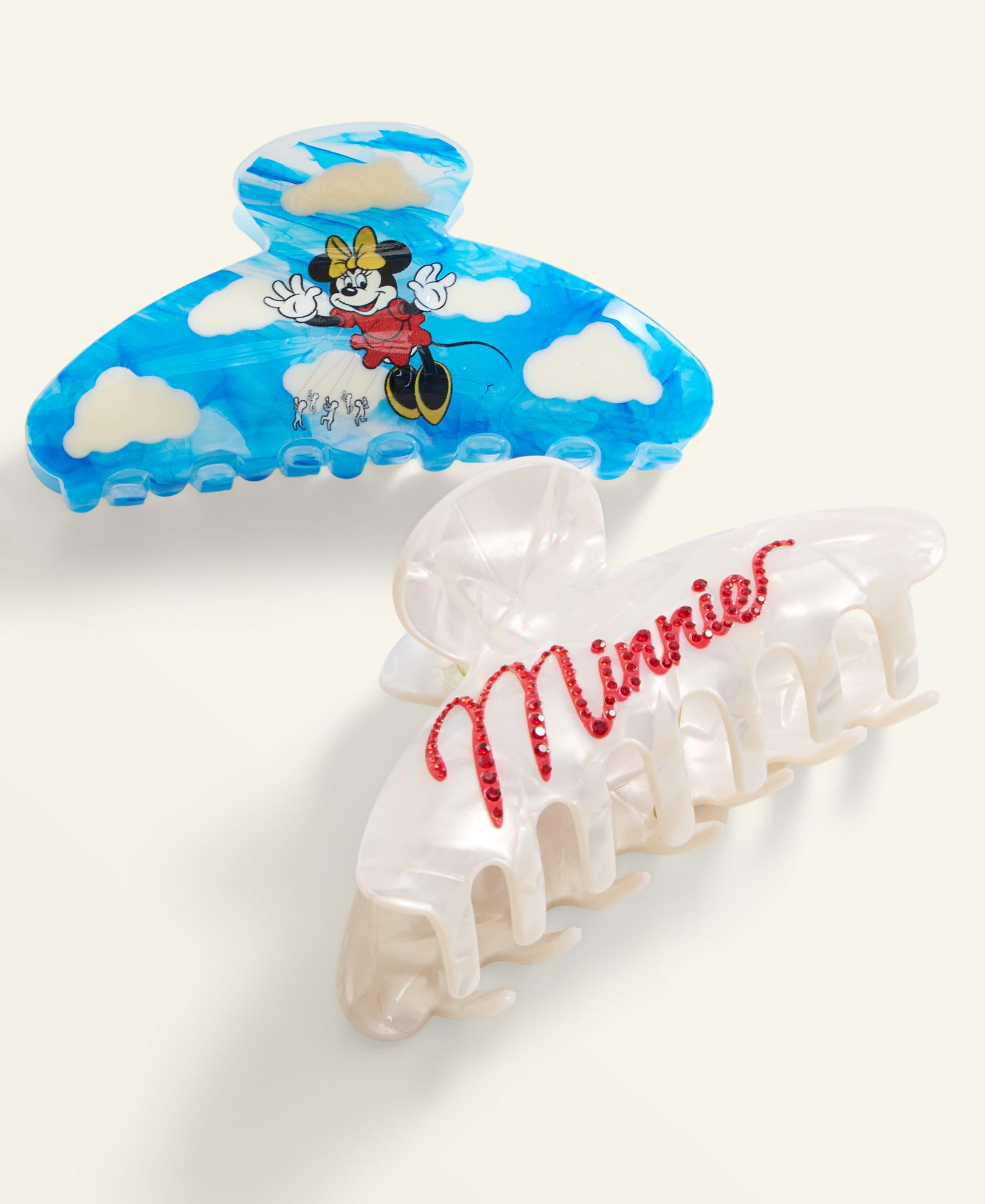 Two festive hair clips from Macy's Disney 2025 Holiday Collection: blue Minnie Mouse and white "Minnie" script, park-inspired style.