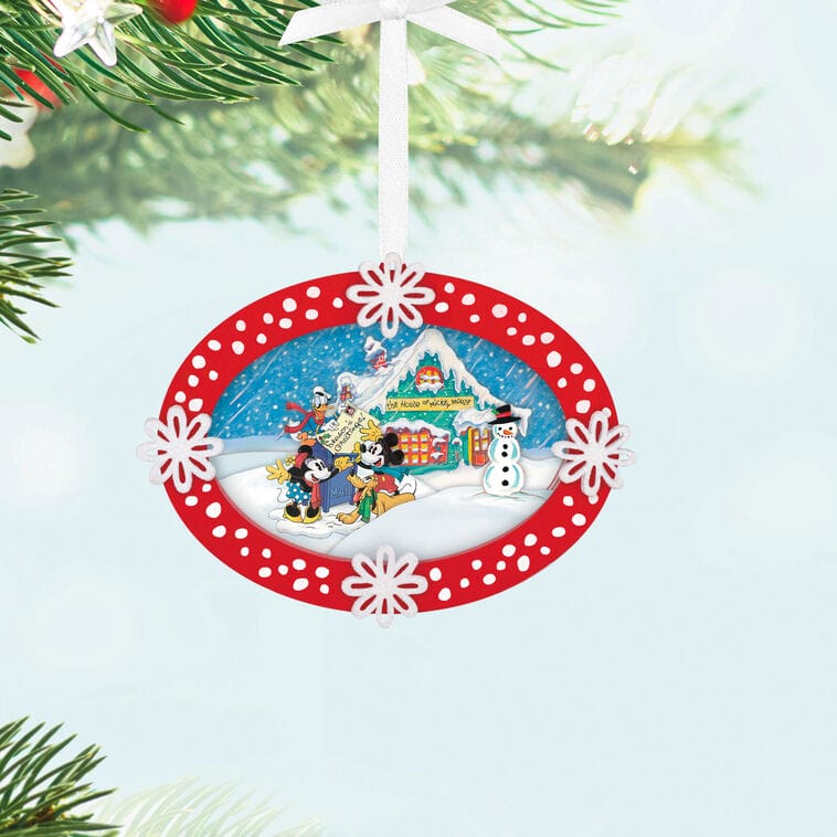 Red and white Hallmark Christmas ornament with Disney characters and a snowman, hanging on a tree branch, reminiscent of park decor.