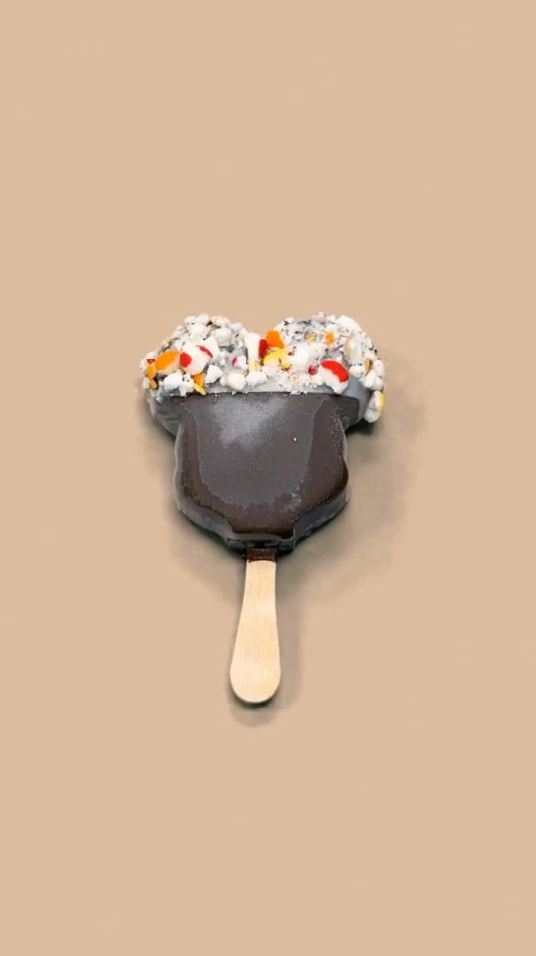 A Mickey's Premium Ice Cream bar with the top half dipped in white chocolate with Skittles POP'd freeze-dried candy.