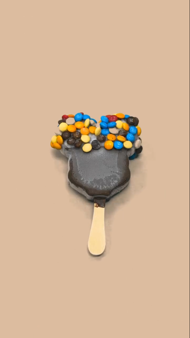 A Mickey's Premium Ice Cream bar with the top half dipped in white chocolate with mini M&Ms.