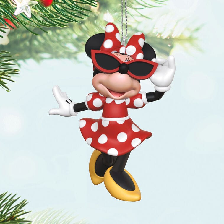 Minnie Mouse in a red polka dot dress and sunglasses as a Disney ornament, hanging from a tree like festive decor at Disney parks.