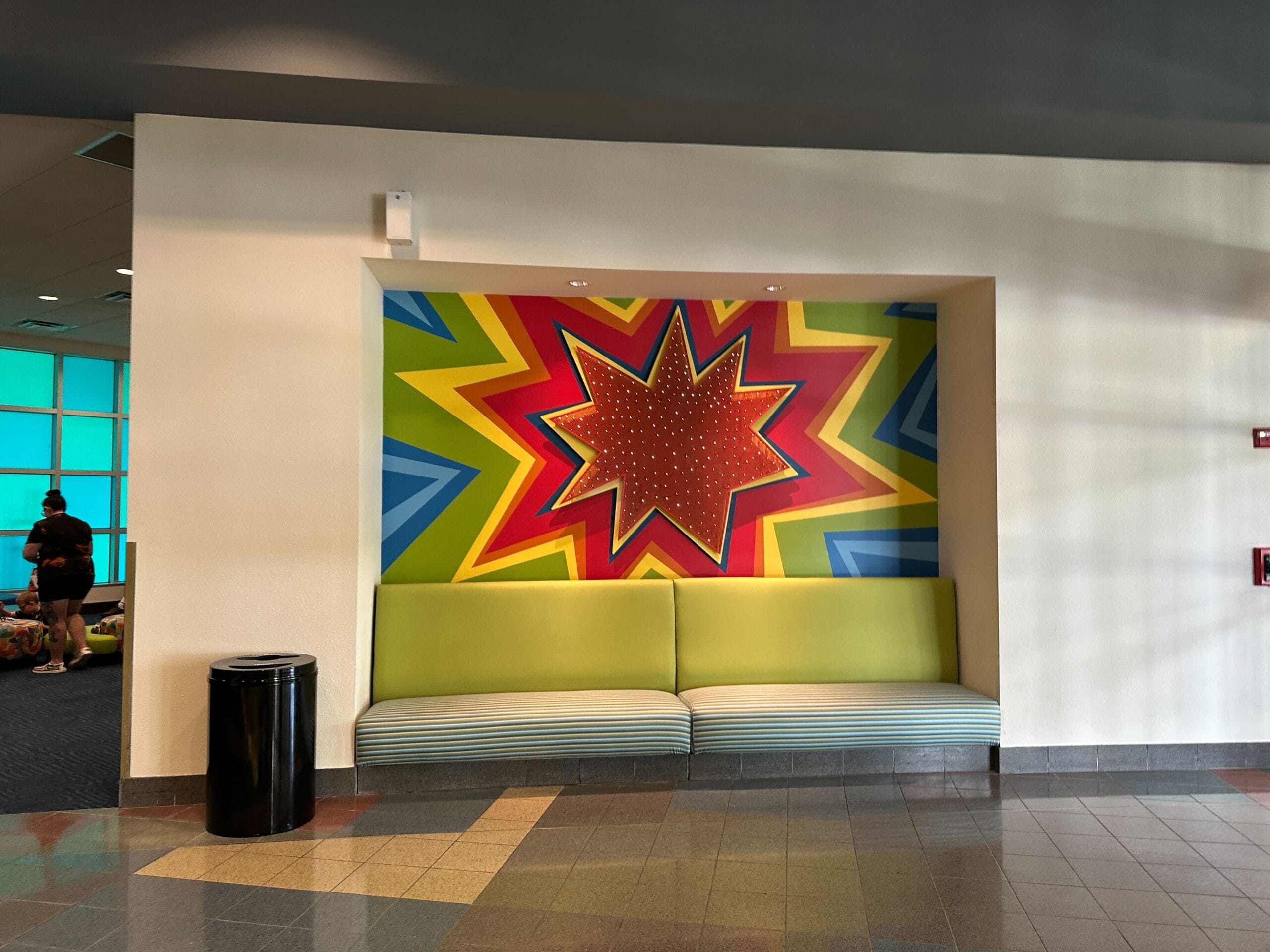A vibrant starburst mural pops behind a green bench in the lobby area at Disney’s Pop Century Resort.