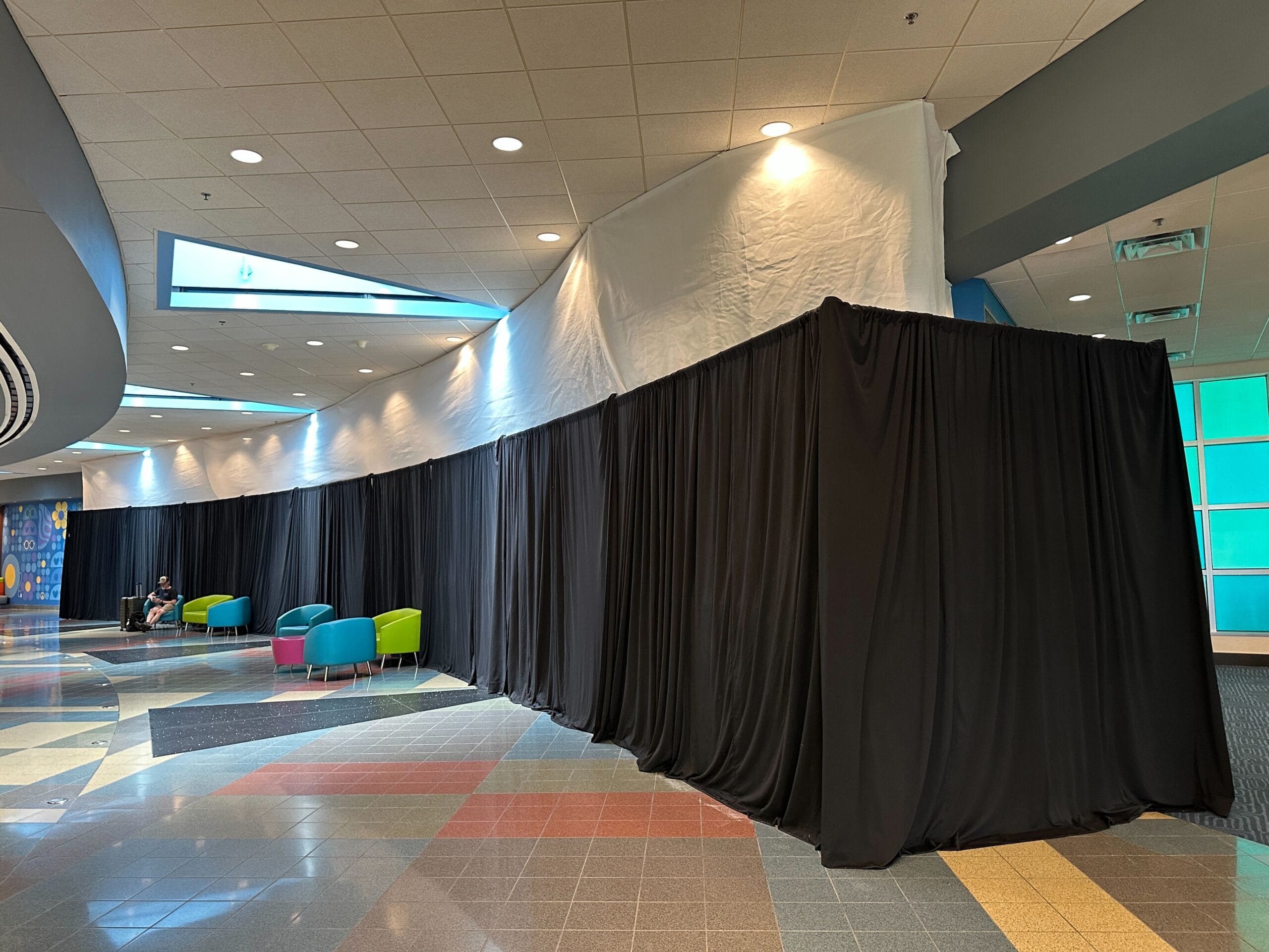 A hallway at Disney's Pop Century Resort has black curtains covering part of the wall, contrasting with the vibrant floors and bright colored lounge chairs.