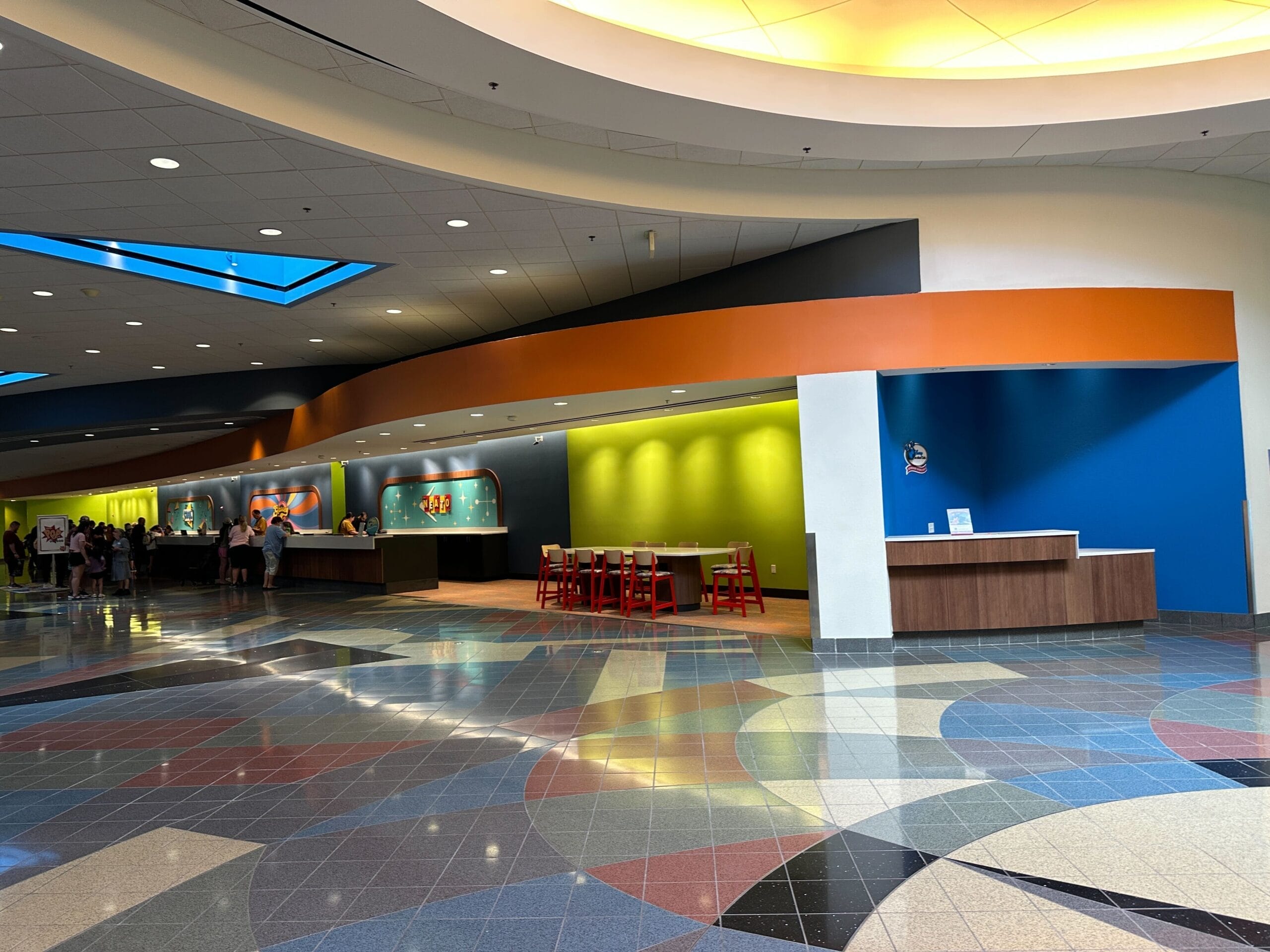 The refurbished lobby of Disney's Pop Century Resort with bright green, blue, and orange accent walls, multicolored swirling tile, and retro signage behind the check-in desks.