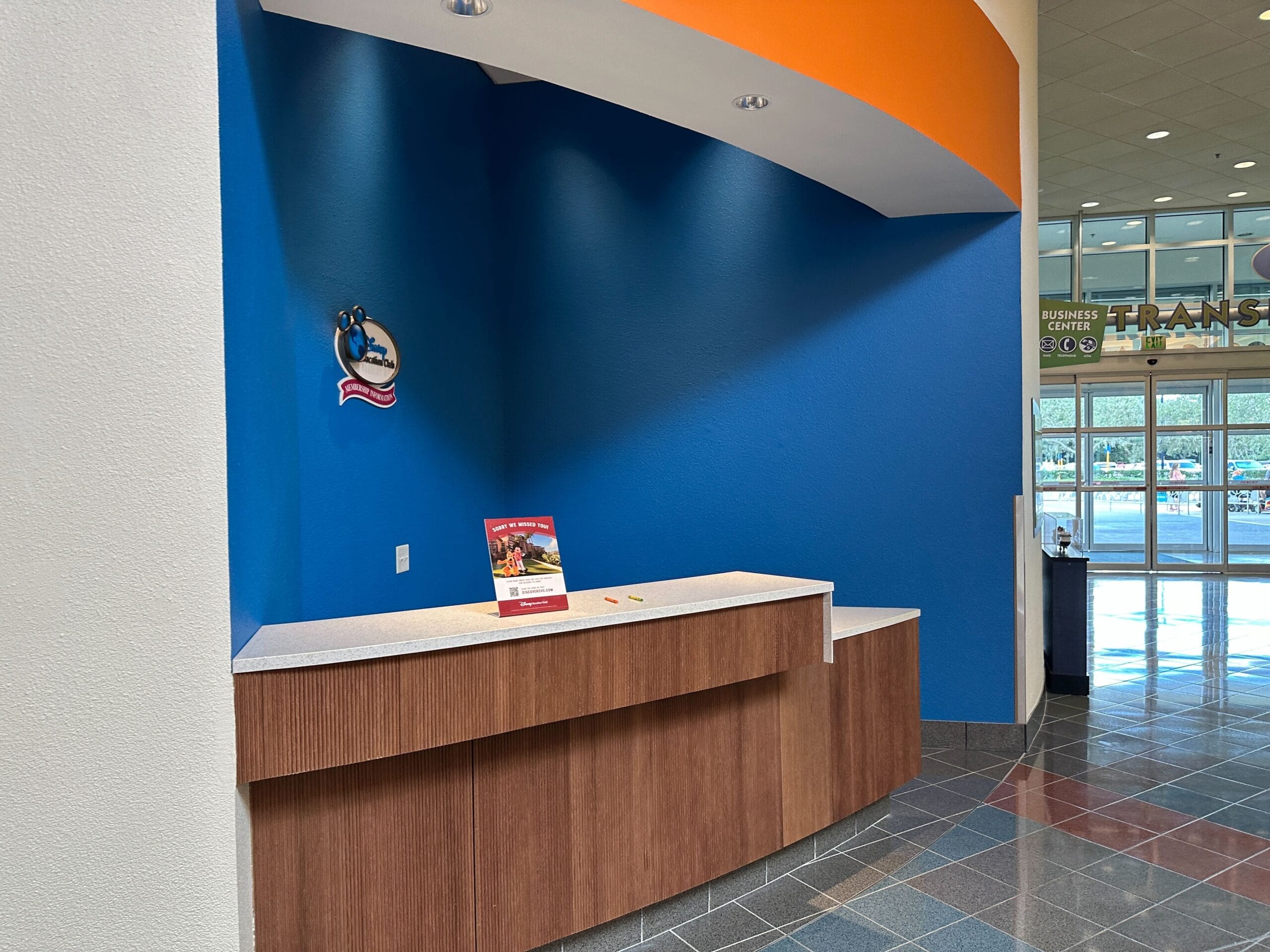 Empty Disney Vacation Club information counter in Disney's Pop Century Resort's lobby, with a bright blue accent wall and pamphlet stand.