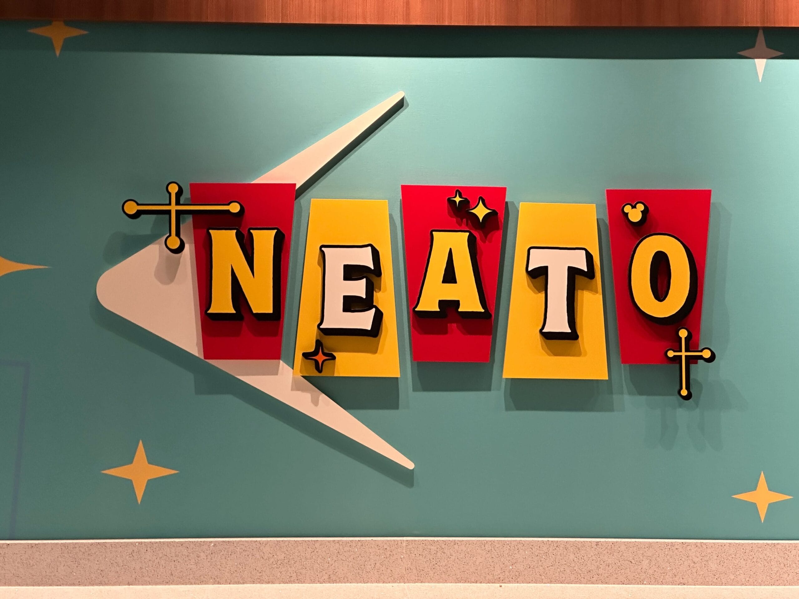 A vibrant retro sign with "NEATO" and starbursts (and a hidden Mickey) pops in red and yellow near the kid's area at Disney's Pop Century Resort.