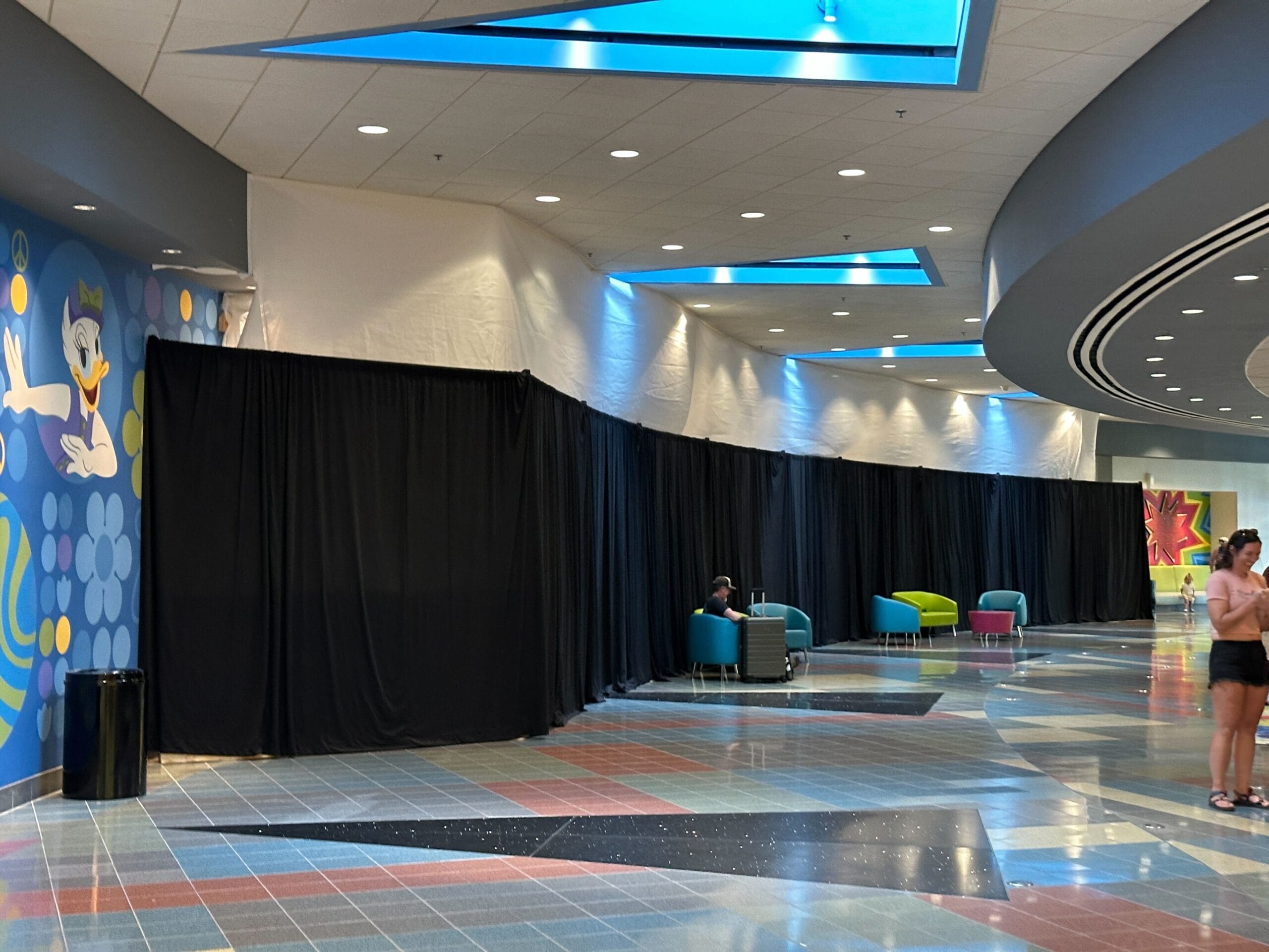 A hallway at Disney's Pop Century Resort has black curtains covering part of the wall, contrasting with the vibrant floors and bright colored lounge chairs.