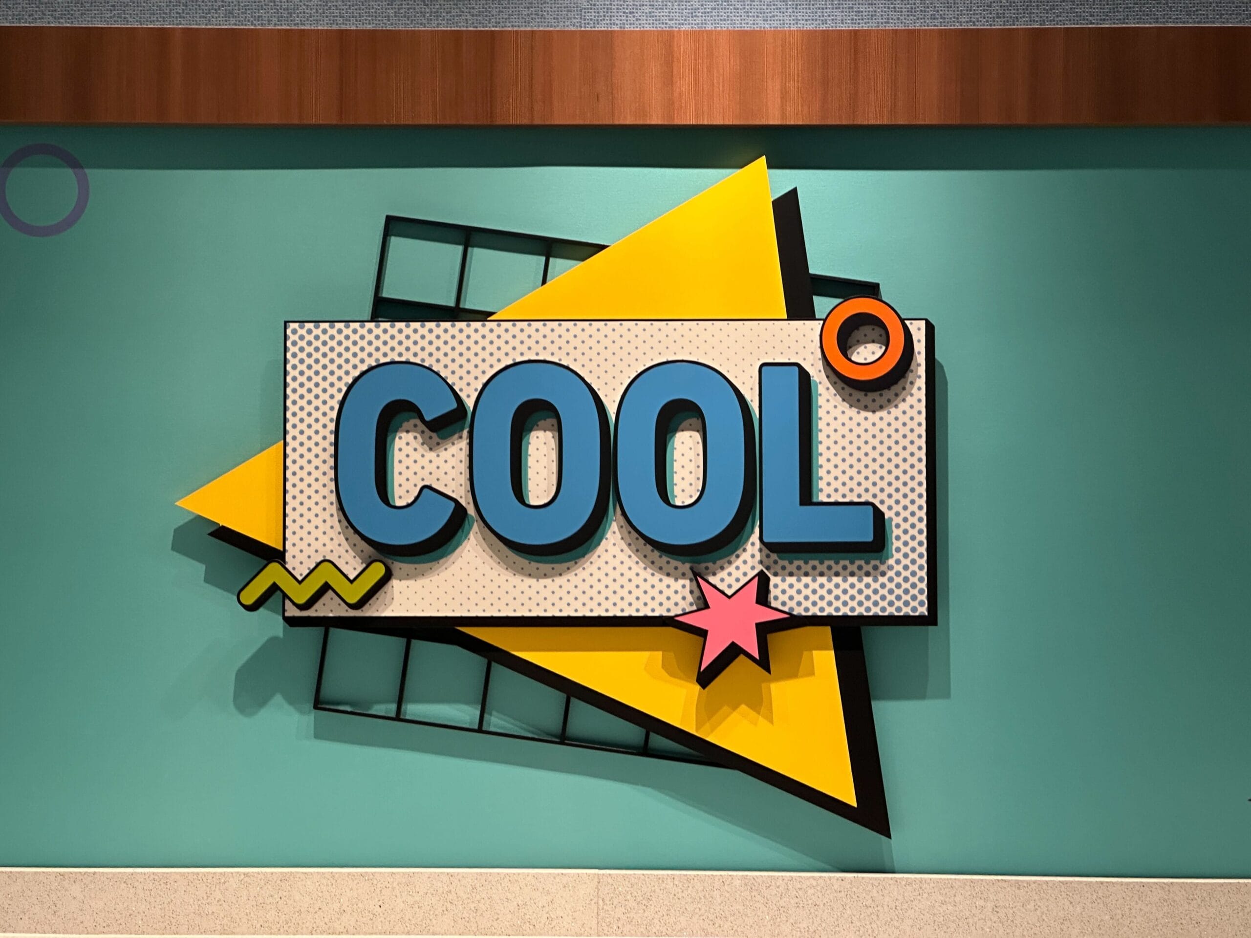 A vibrant wall of bold geometric shapes says "COOL" near the check-in area at Disney’s Pop Century Resort.