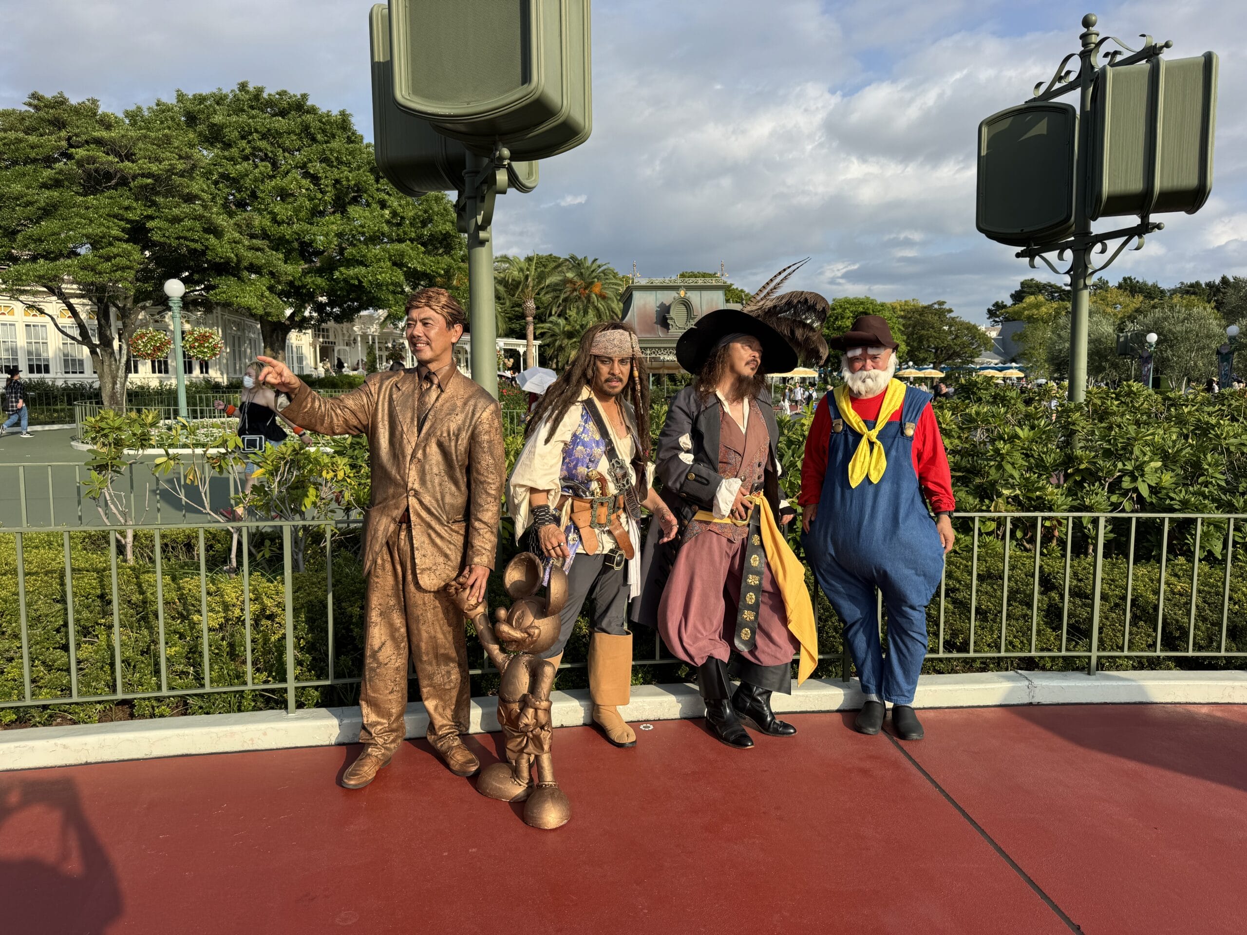 Four people in elaborate costumes pose outdoors by lush trees, evoking Tokyo Disney Resort’s festive Halloween spirit together.