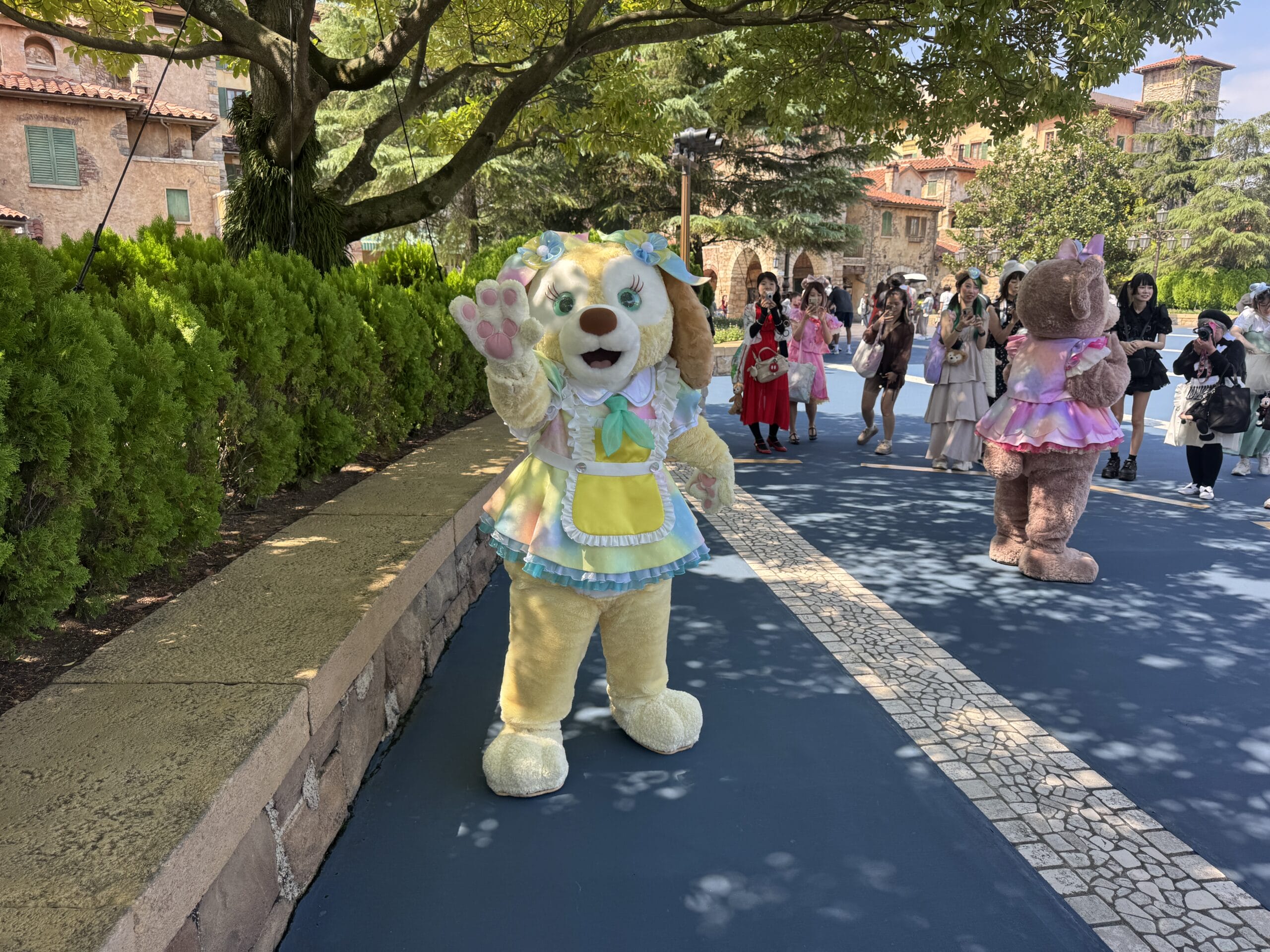A person in a dog costume waves on a sunny path at Tokyo Disney Resort, where Halloween costumes fill the walkways—not far from Cinderella Castle, which has its own unique style compared to the Walt Disney World castle.