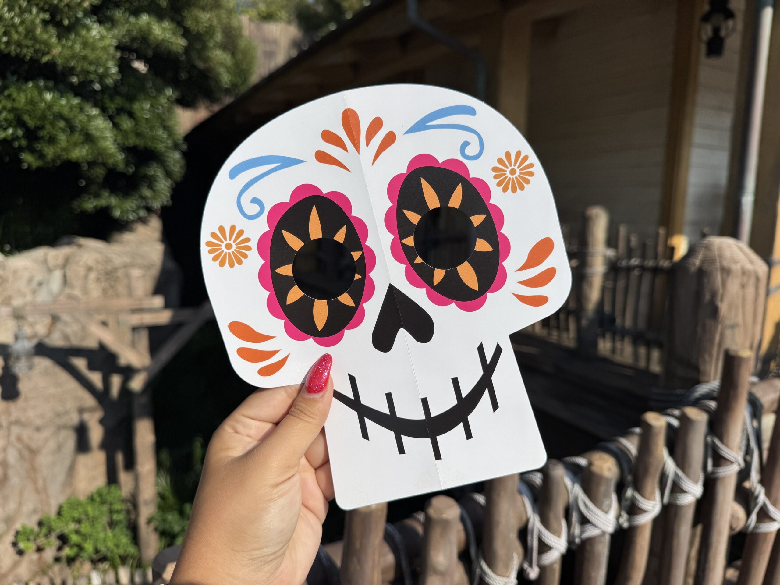 A hand holds a vibrant Day of the Dead skull mask with flowers, echoing festive Disney park Halloween décor near castle celebrations.