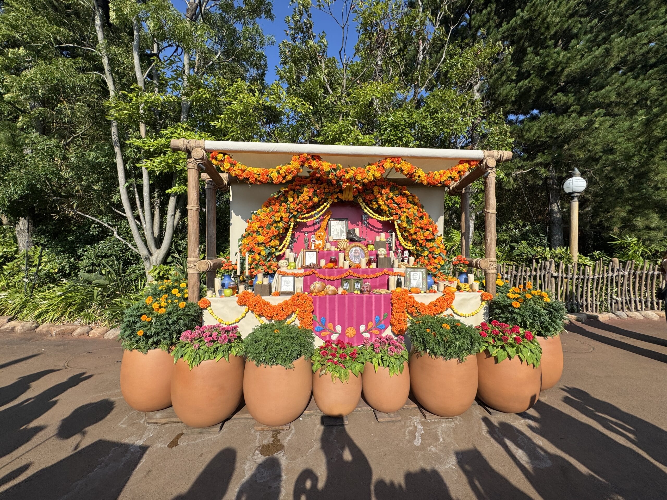 A colorful Día de los Muertos altar with marigolds and candles, framed by lush potted plants, evokes festive Disney park decor.
