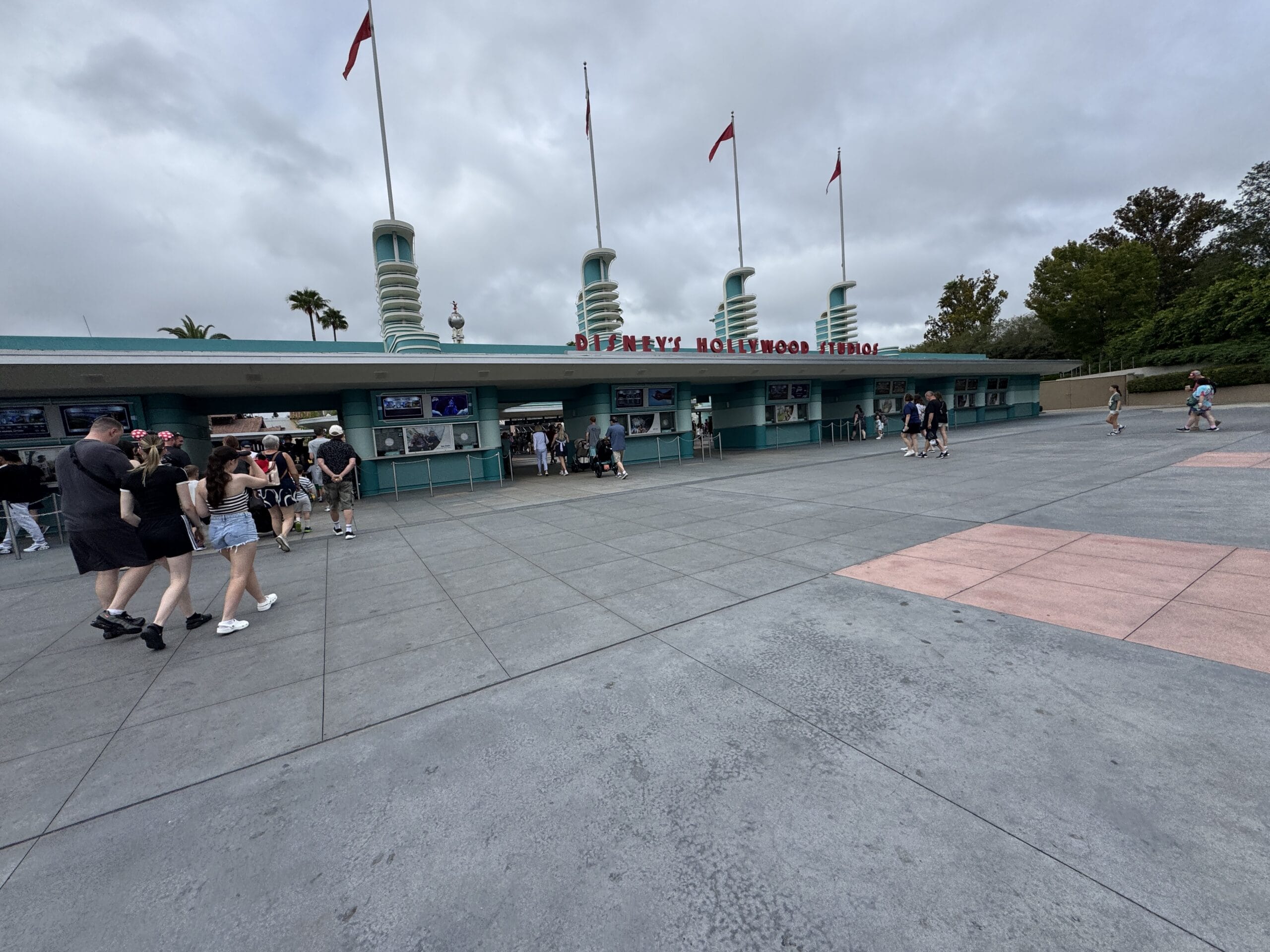 Guests pass by the art deco entrance of Disney’s Hollywood Studios, decorated with red Halloween flags—no castle like at Magic Kingdom.
