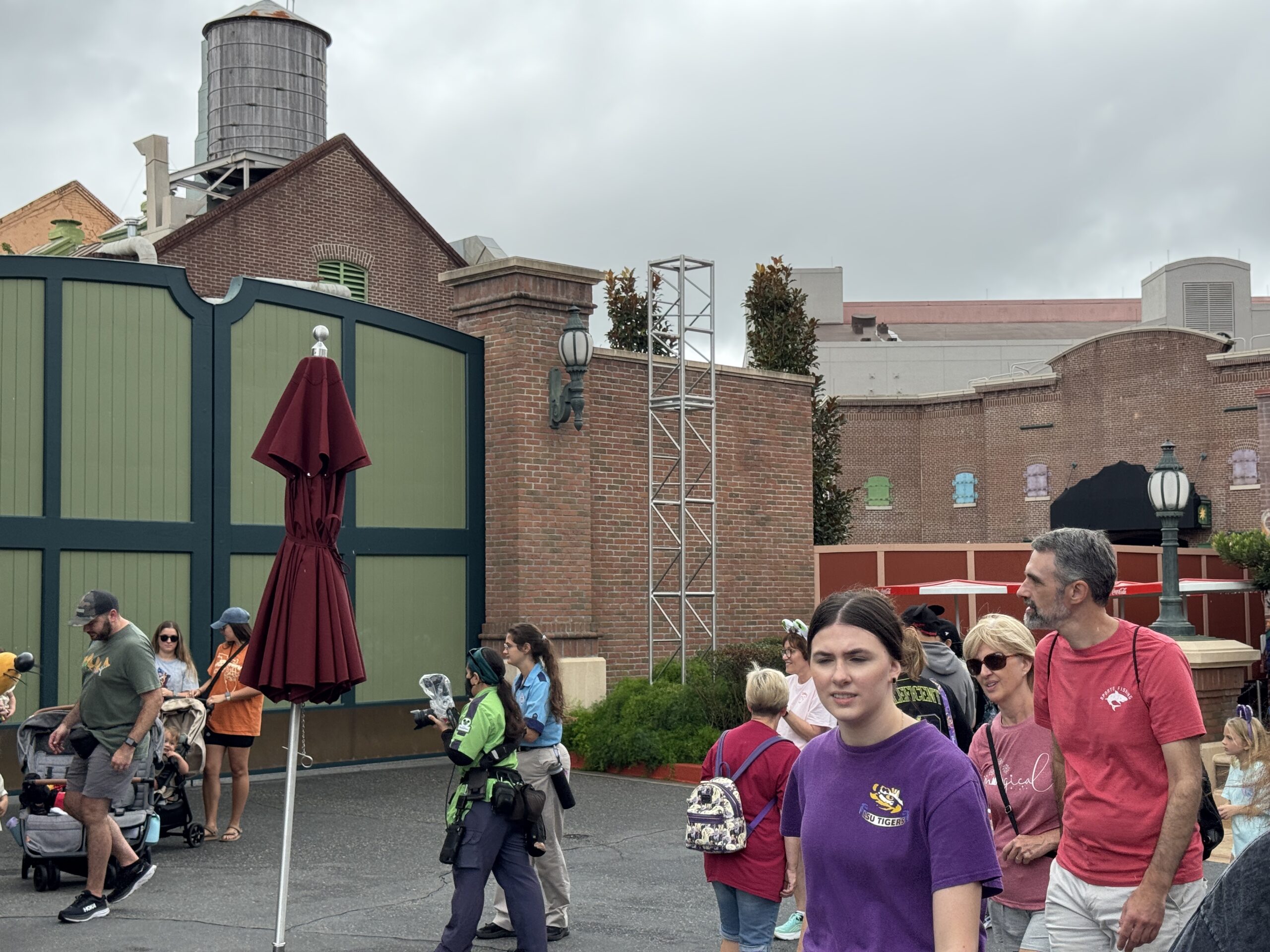 Guests stroll by brick buildings and a closed red umbrella on a cloudy day at Tokyo Disney Resort, with no castle in view to compare.
