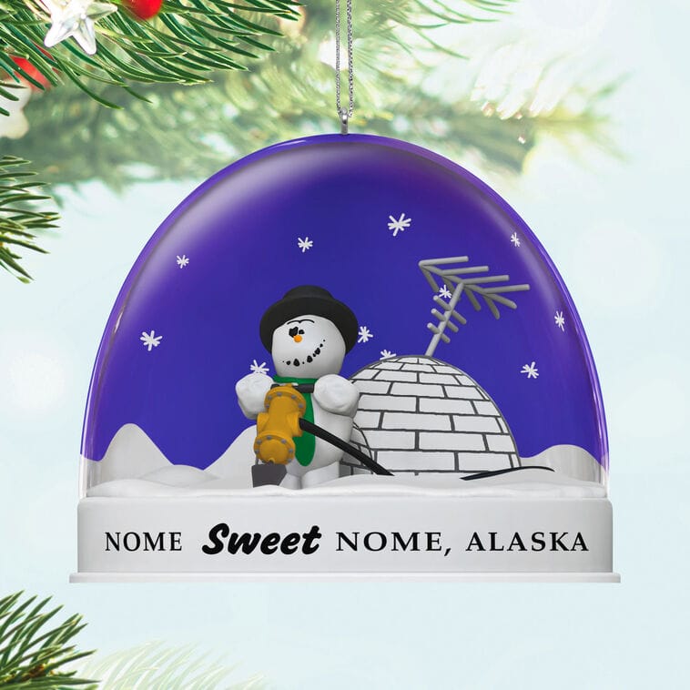 Festive Disney-style ornament featuring a snowman and igloo, labeled "Nome Sweet Nome, Alaska," hanging on a tree branch.