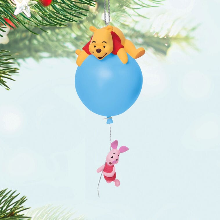 Winnie the Pooh rests on a blue balloon ornament above Piglet on a Hallmark Disney Keepsake tree, reminiscent of Main Street decor.