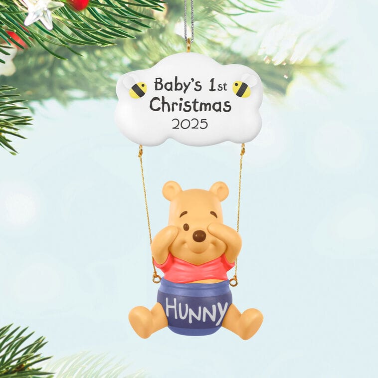 Winnie the Pooh with a "hunny" pot, "Baby's 1st Christmas 2025" Hallmark Disney ornament hanging on the tree. No castle shown.