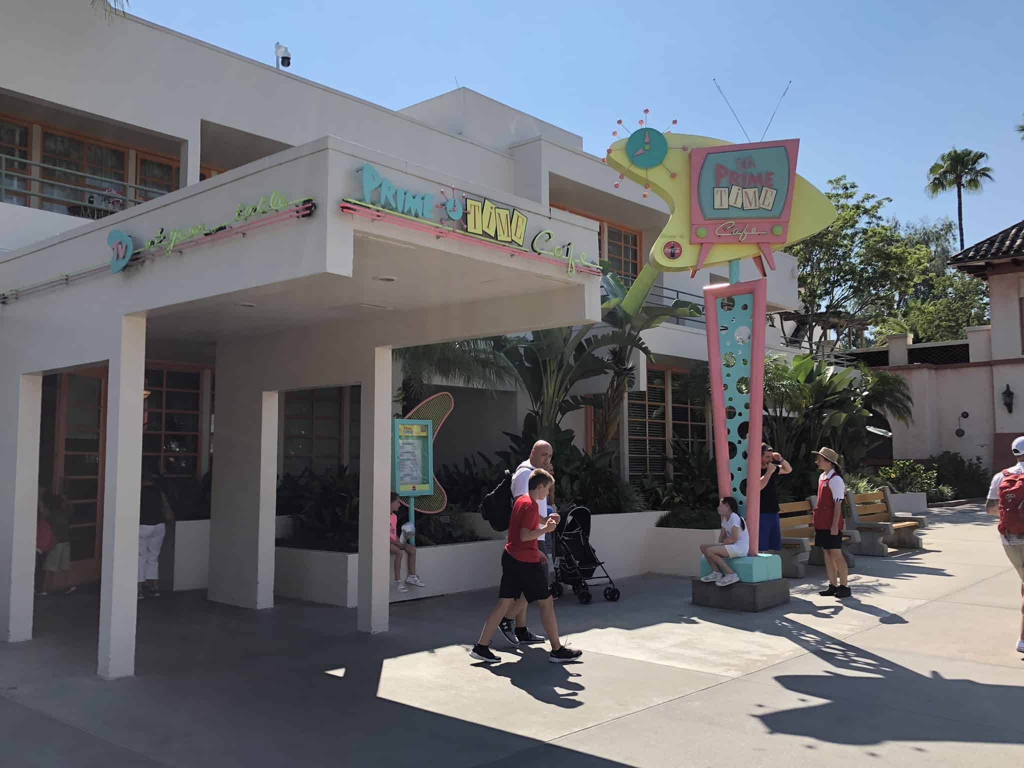 Guests stroll past the retro 50’s Prime Time Café at Disney’s Hollywood Studios, with its colorful sign and outdoor patio seating.