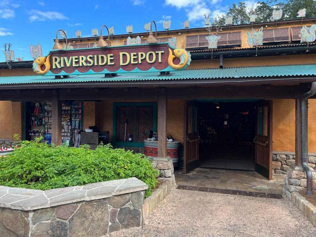 Entrance to Riverside Depot at a Disney park, featuring owl decor and Mickey Mouse items inside, set beneath a clear blue sky.
