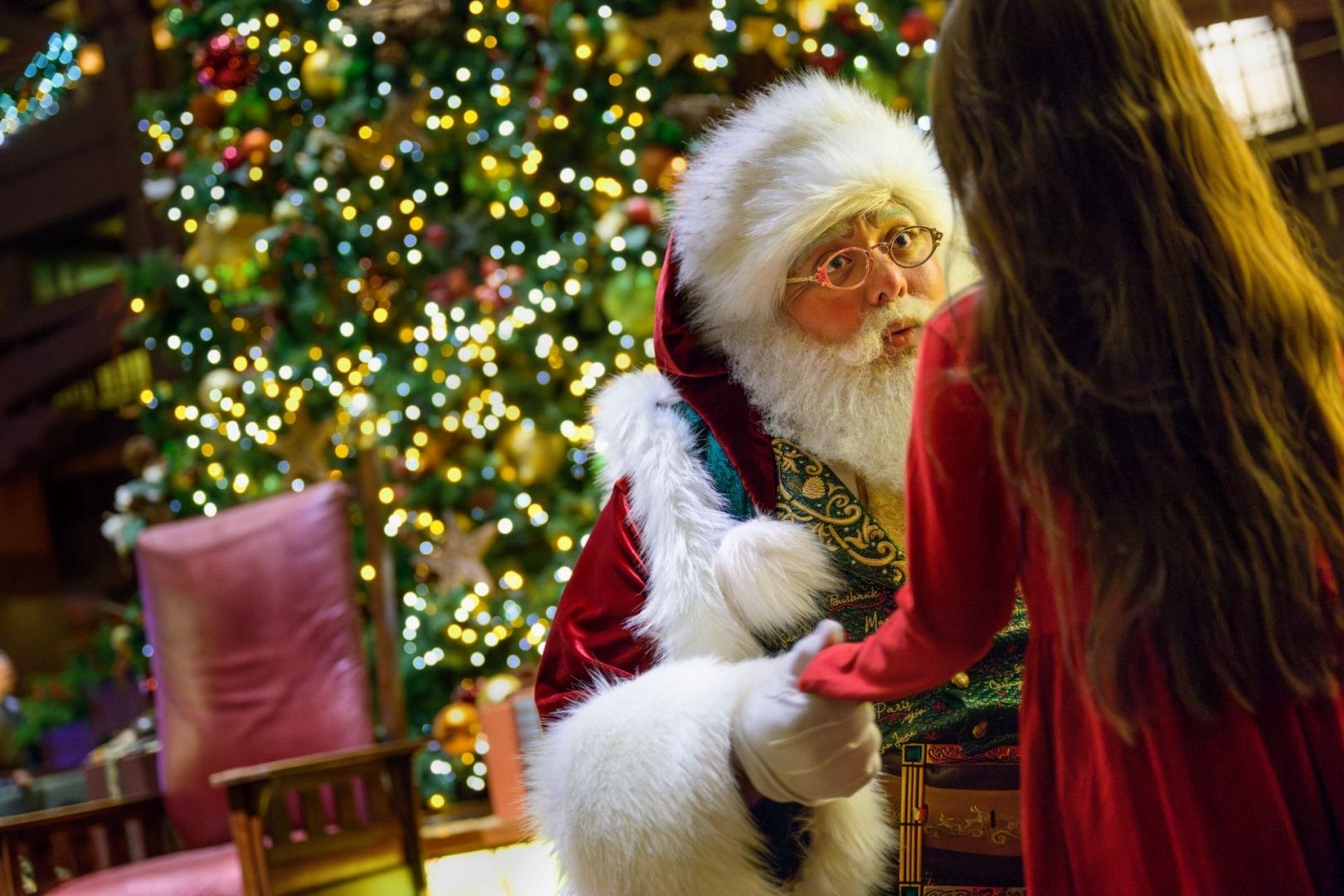 Santa Claus holds a young girl’s hand in front of a Christmas tree at a Disney park, adding holiday magic to the Daily Recap moment.