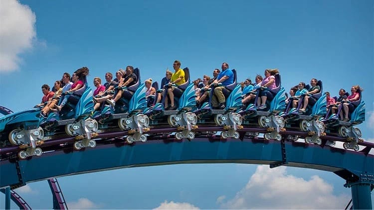 Guests race along the Mako Coaster at SeaWorld, arms up under blue skies.