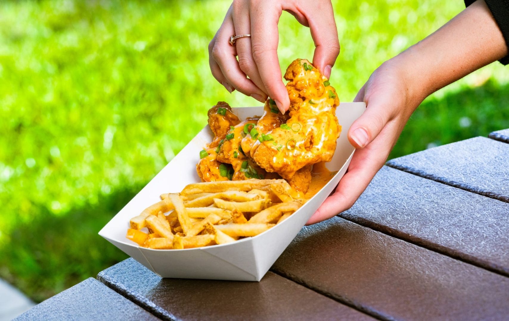 A person picks up saucy chicken strips from a tray with French fries on an outdoor table at Disney World.