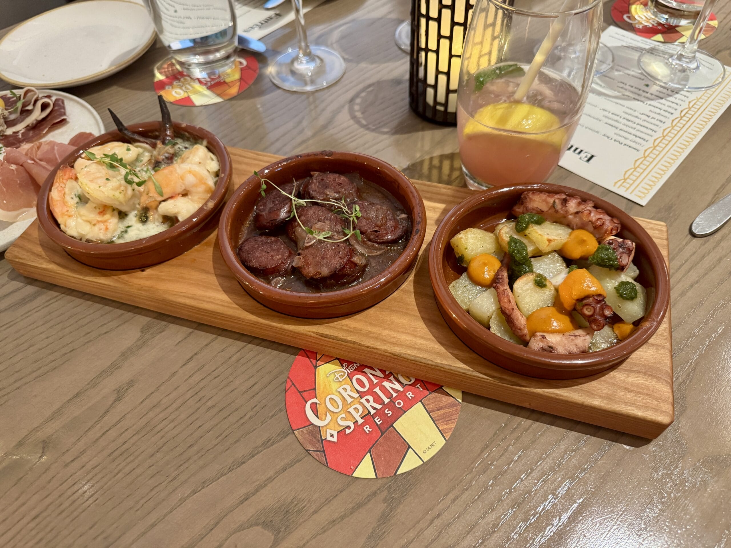 Three small bowls of Toledo tapas—shrimp, chorizo, and octopus—served on a wooden board at a restaurant table.