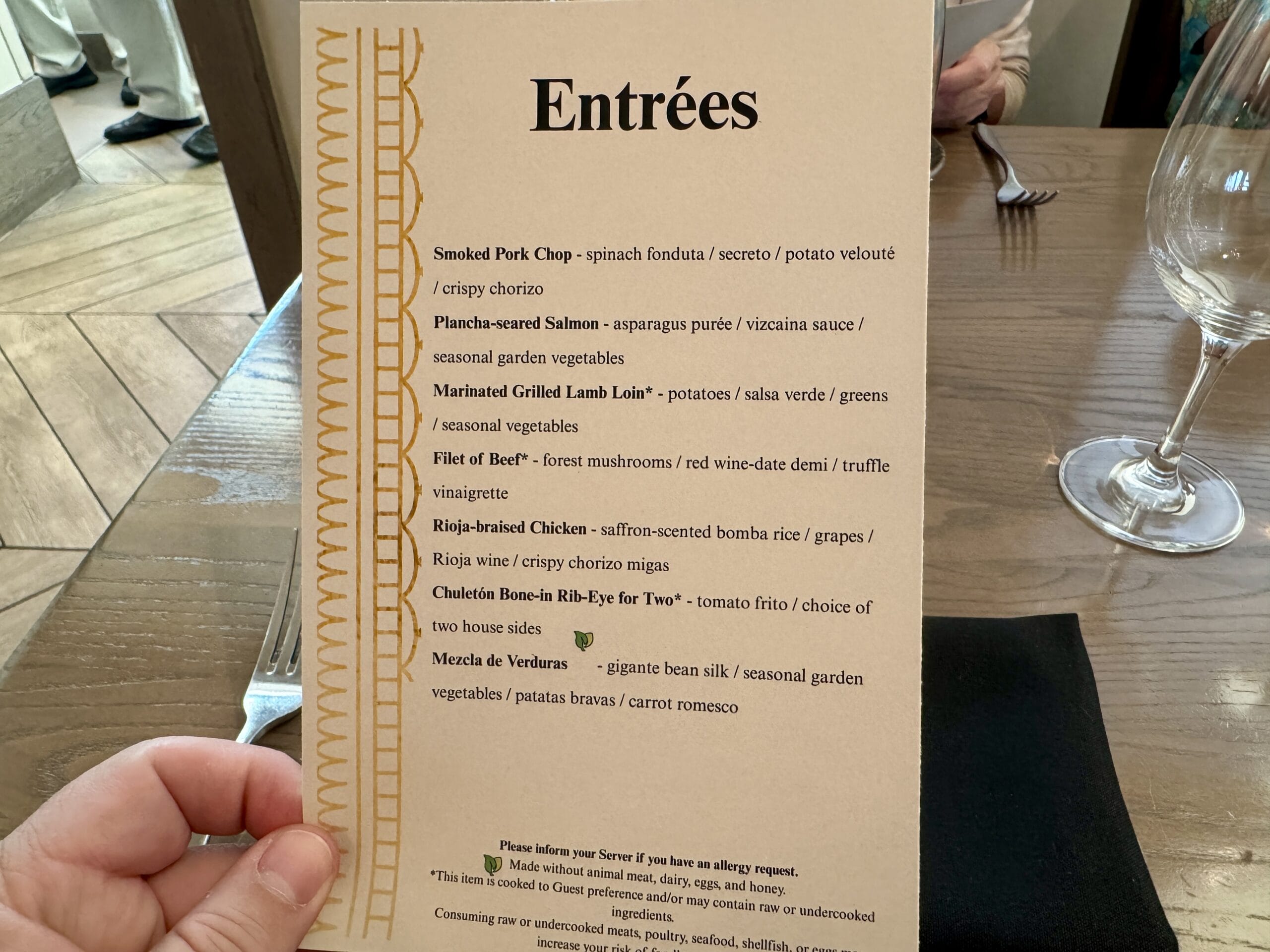 Hand holding a restaurant menu of entrées, featuring steak, seafood, pork chop, chicken, and vegetable dishes.