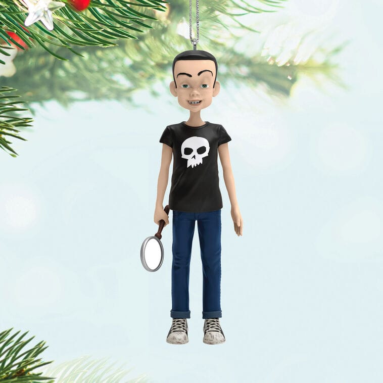 A Hallmark Keepsake Ornament of a cartoon boy in a skull shirt with magnifying glass hangs on a Christmas tree, like Main Street decor at Disneyland.