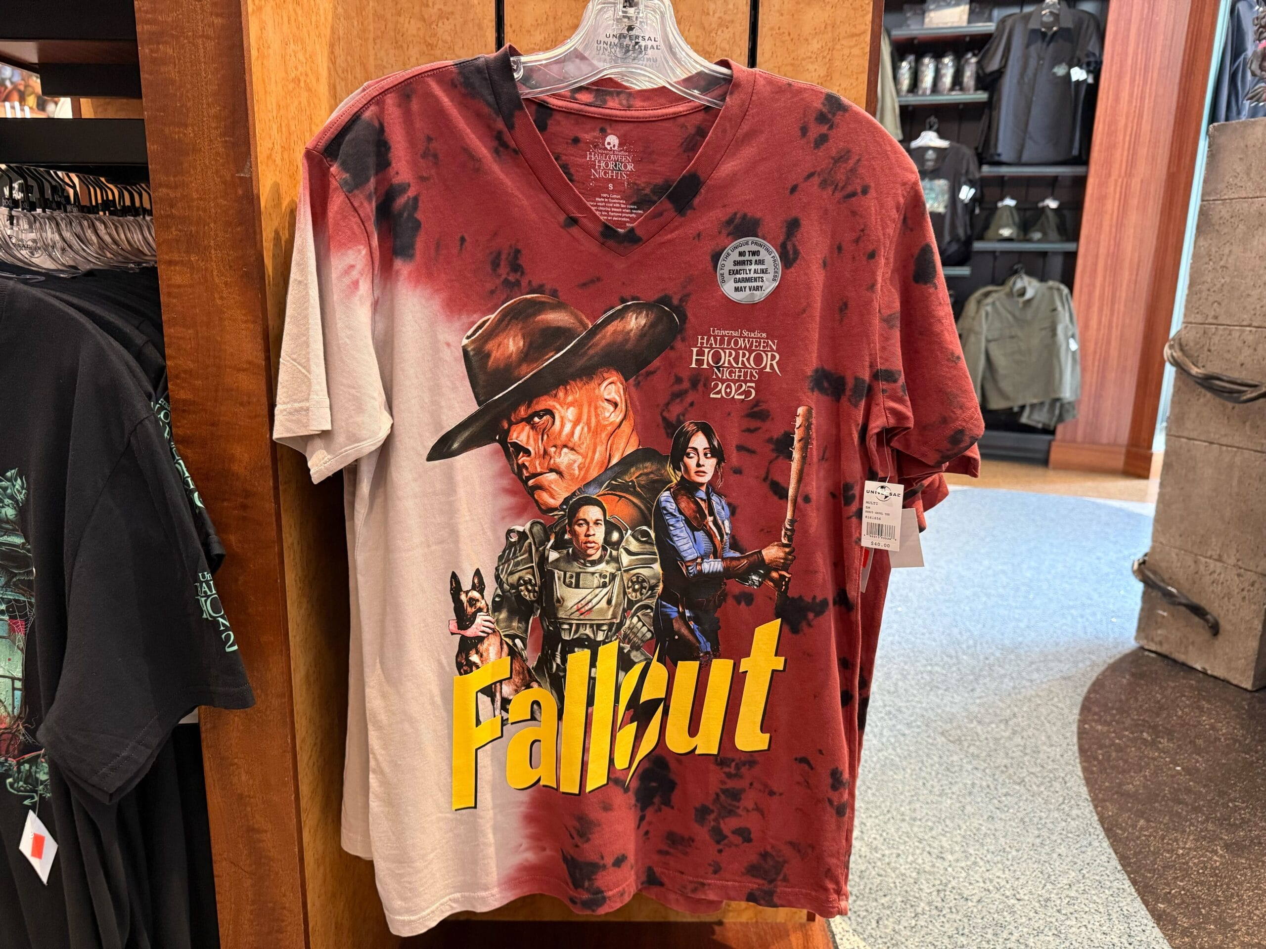 A 2025 Halloween Horror Nights “Fallout” V-neck T-shirt featuring a red and black tie-dye design and graphics of Dogmeat, Titus, the Ghoul, and Lucy.
