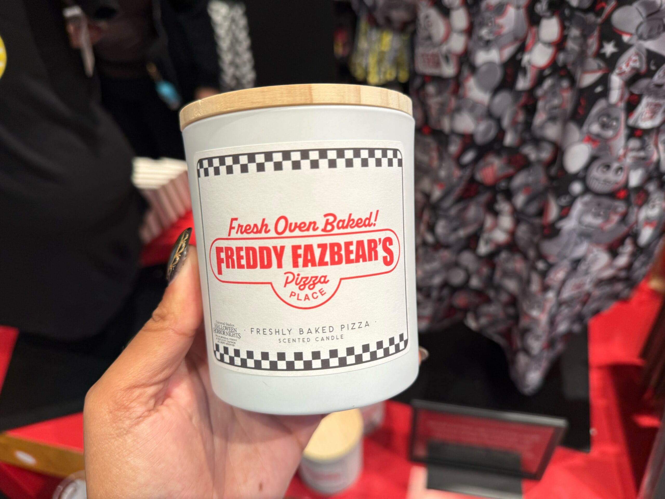 A hand holds a white "Freddy Fazbear's Pizza Place" lidded candle car, 2025 Halloween Horror Nights merch.
