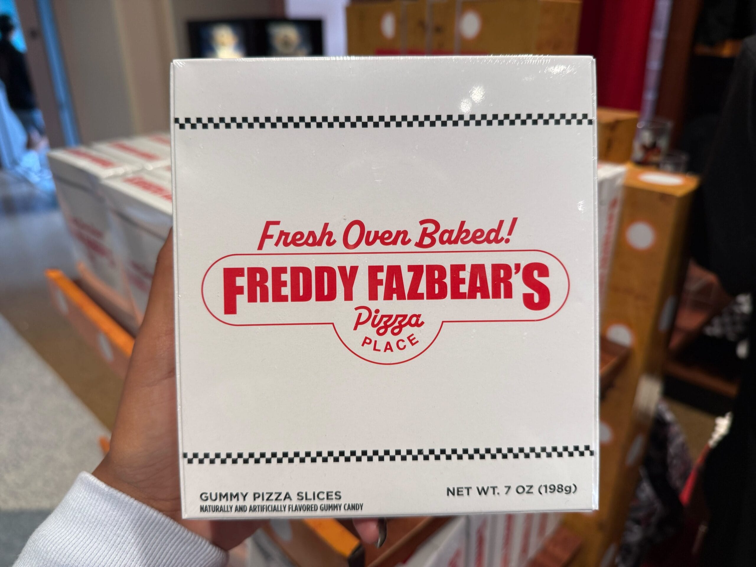 A hand holds a white "Freddy Fazbear's Pizza Place" box from Universal.