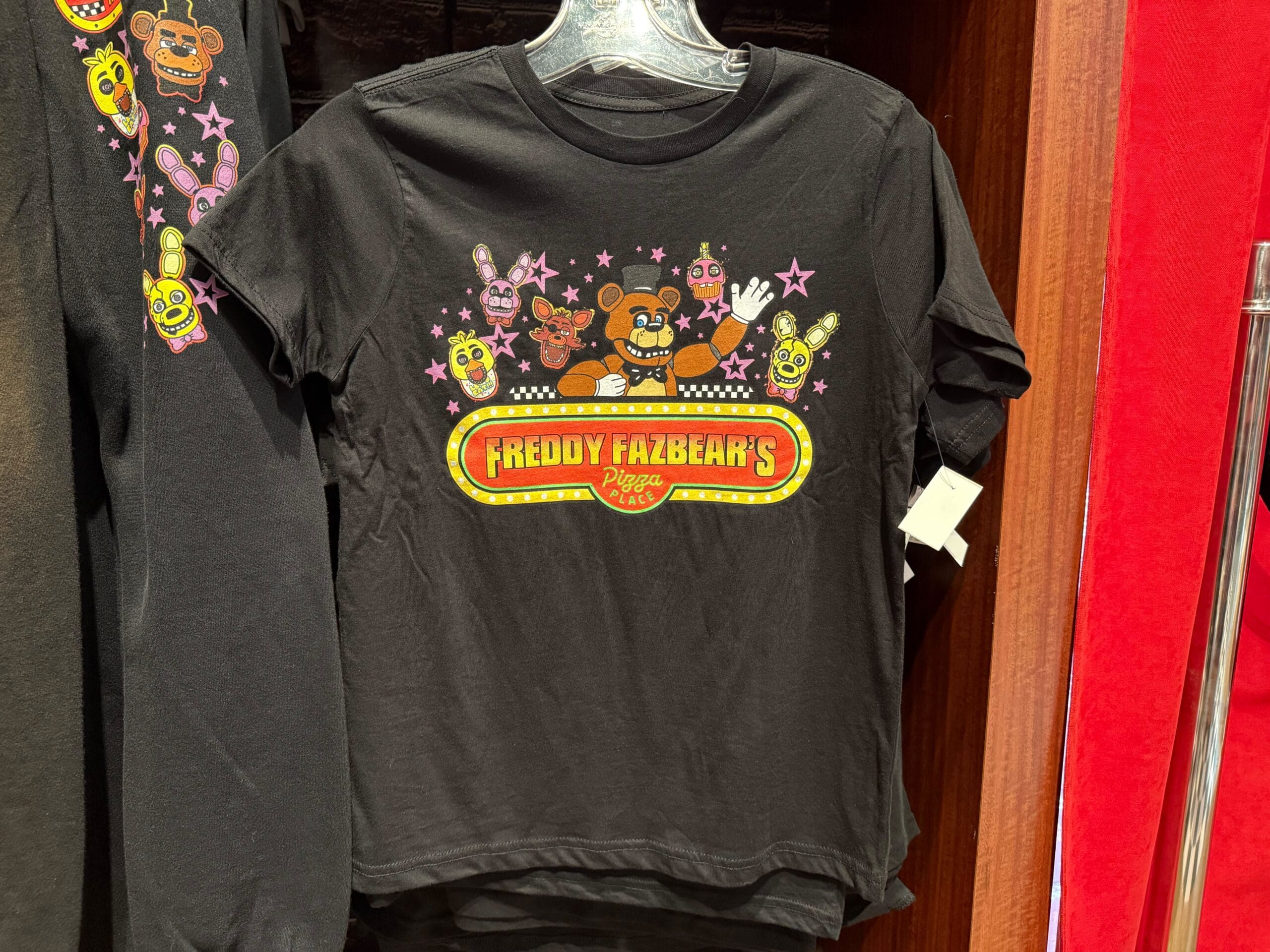 Black T-shirt with Freddy Fazbear’s Pizza Place logo and cartoon icons of the animatronics with pink stars.