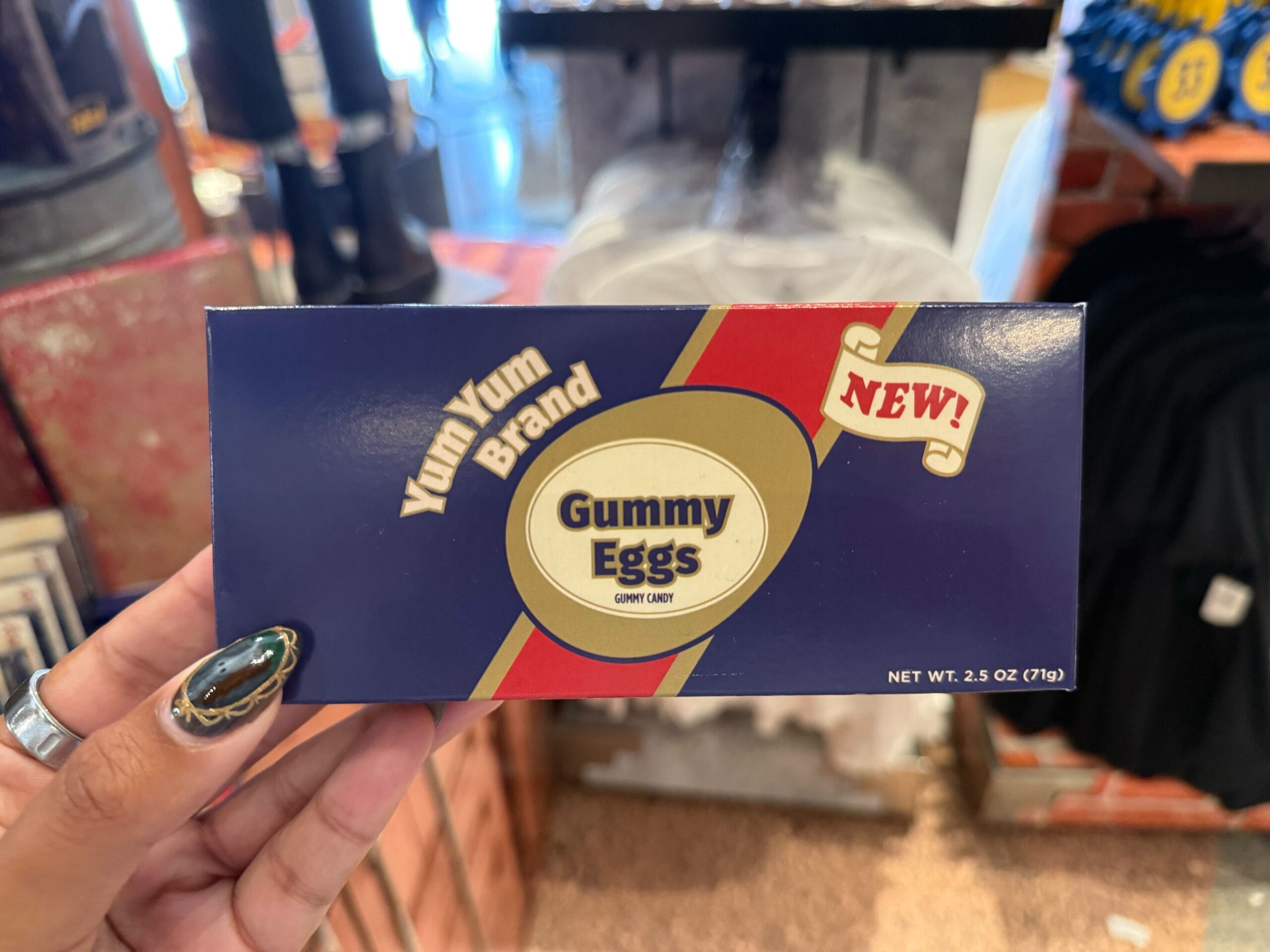 A hand holds a box of Yum Yum Brand Gummy Eggs labeled "NEW!" at a Universal Studios 2025 merchandise display.