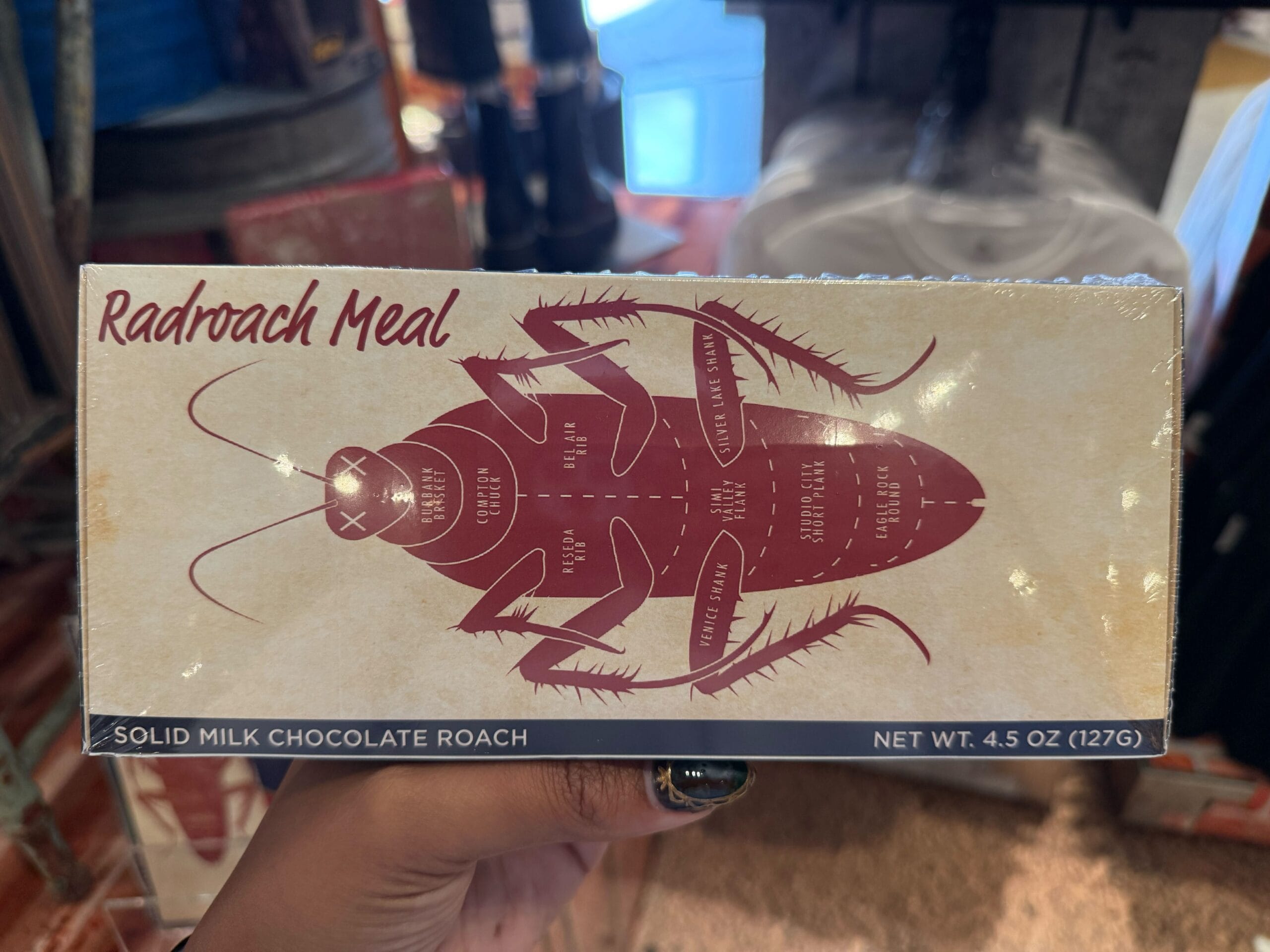 A hand holds a "Radroach Meal" box, 2025 Universal Studios treat with roach-shaped milk chocolate.
