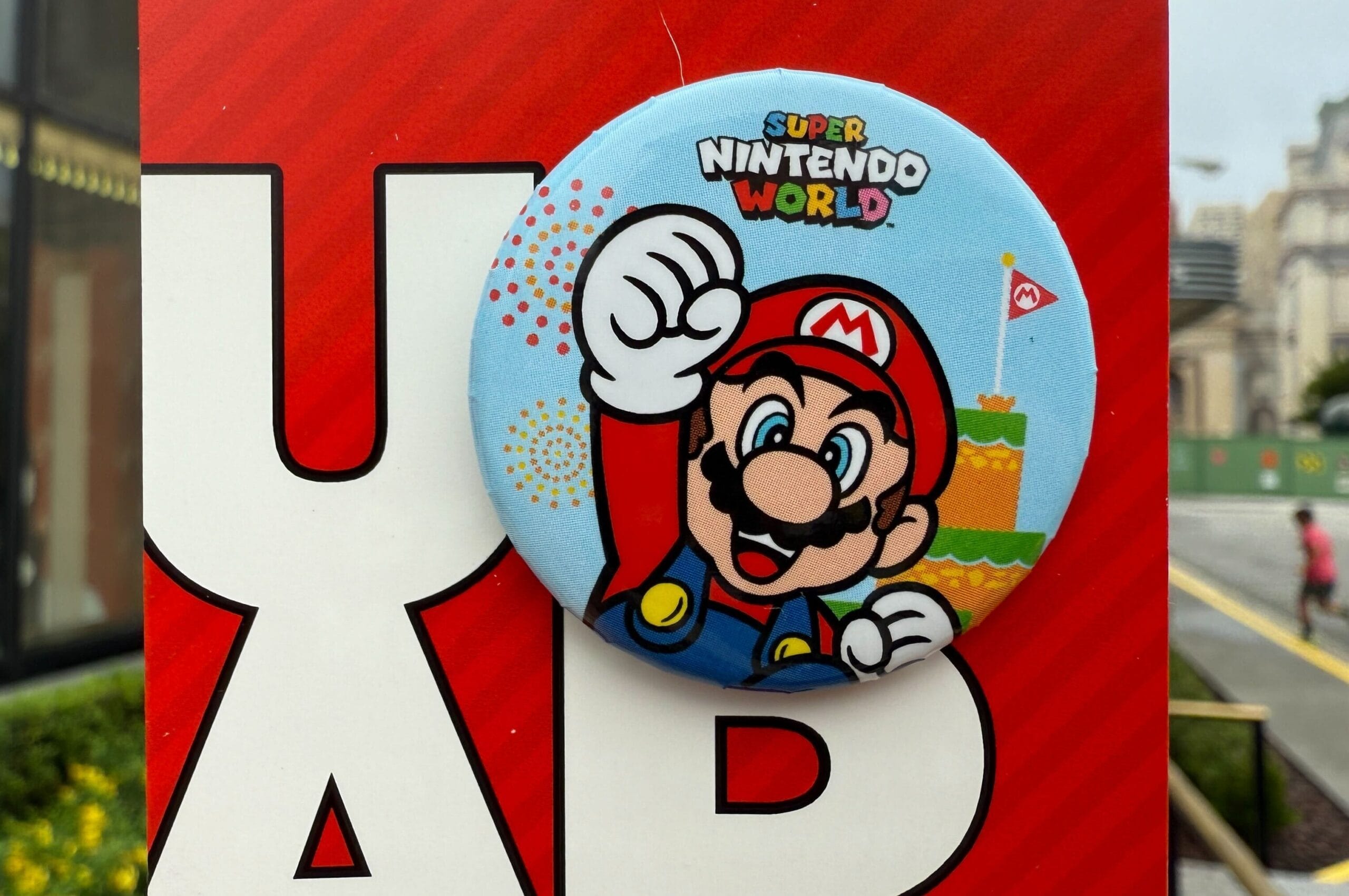 A Super Nintendo World Mario button is pinned on a red and white sign at Universal Orlando, not Disney, with no castle in sight.