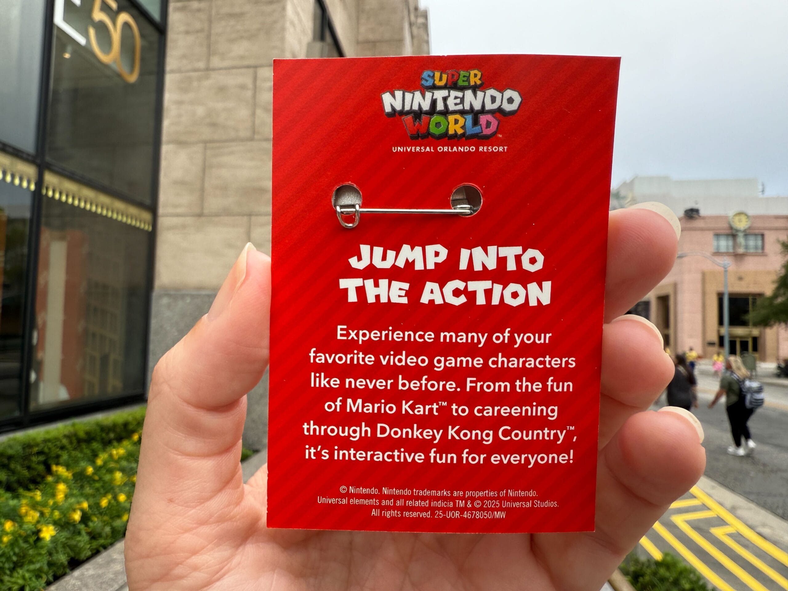 A hand holds a red Super Nintendo World card outside Universal Orlando Resort, distinctly non-Disney with no castle like Cinderella’s nearby.