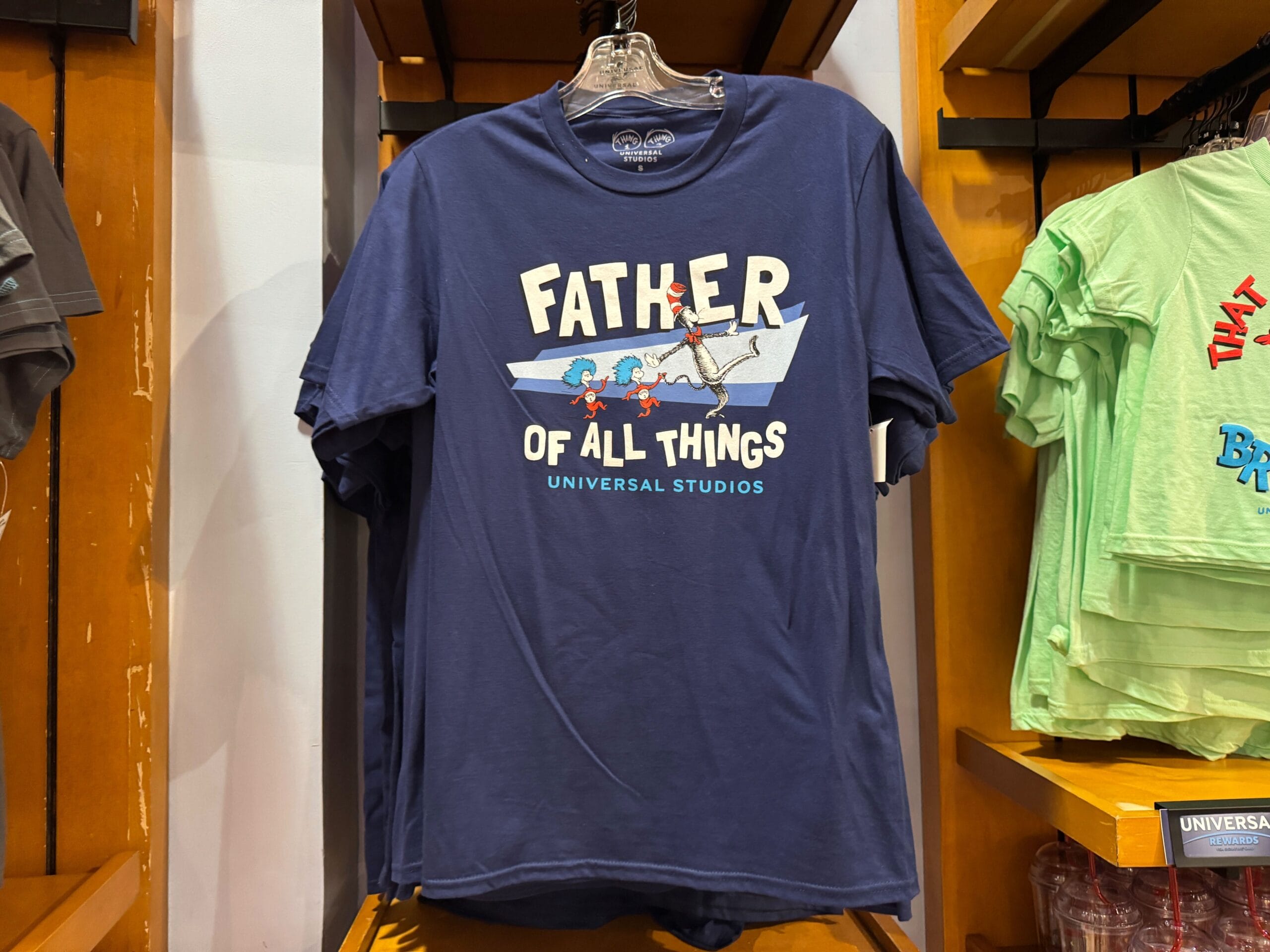 Navy blue Dr. Seuss tee with "Father of All Things" and Thing 1 & Thing 2, seen on a rack—not Disney Parks or castle apparel.
