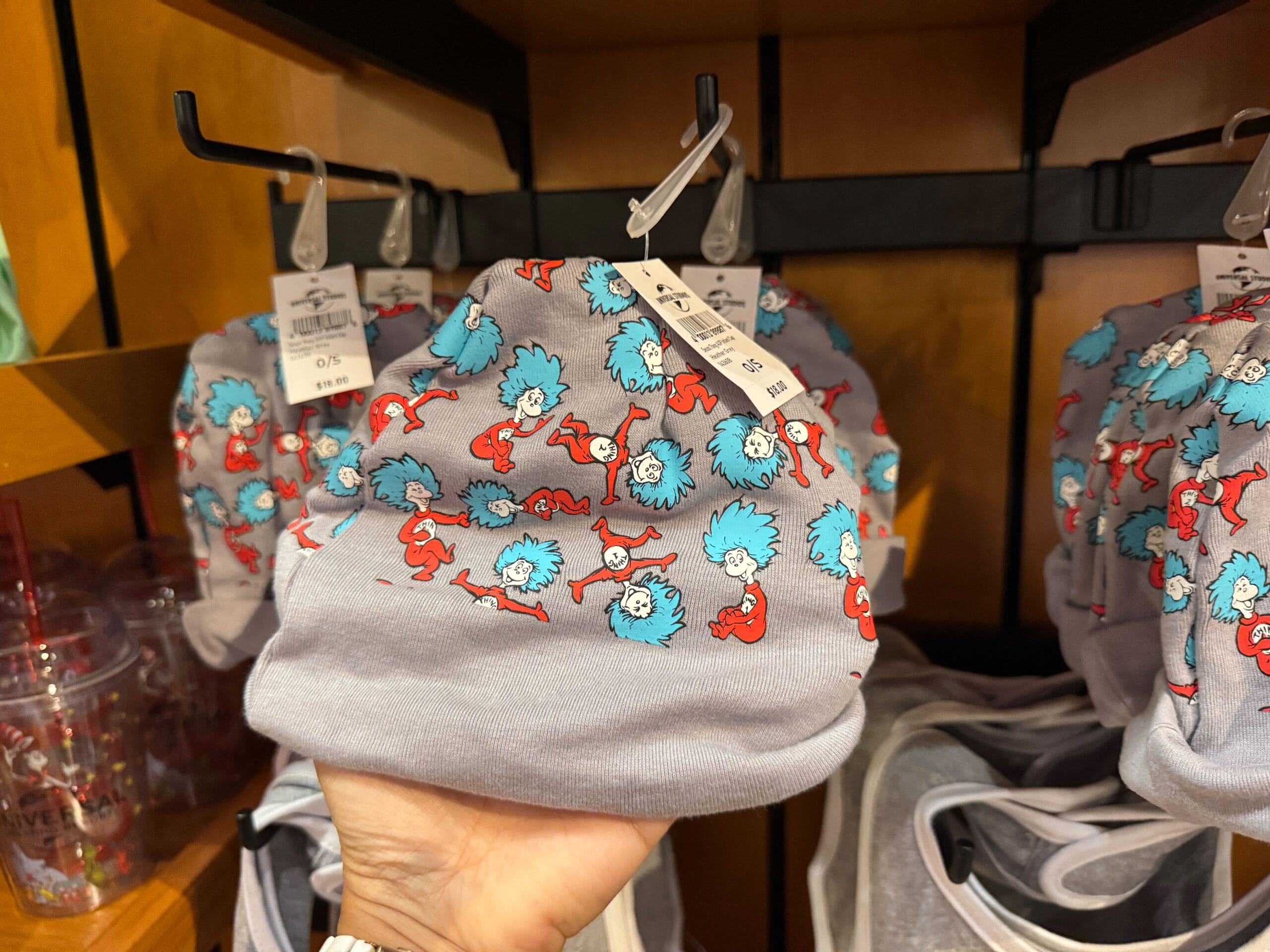 A hand holds a gray baby hat featuring Thing 1 & Thing 2, Dr. Seuss characters, at Universal Studios—not a Disney park.