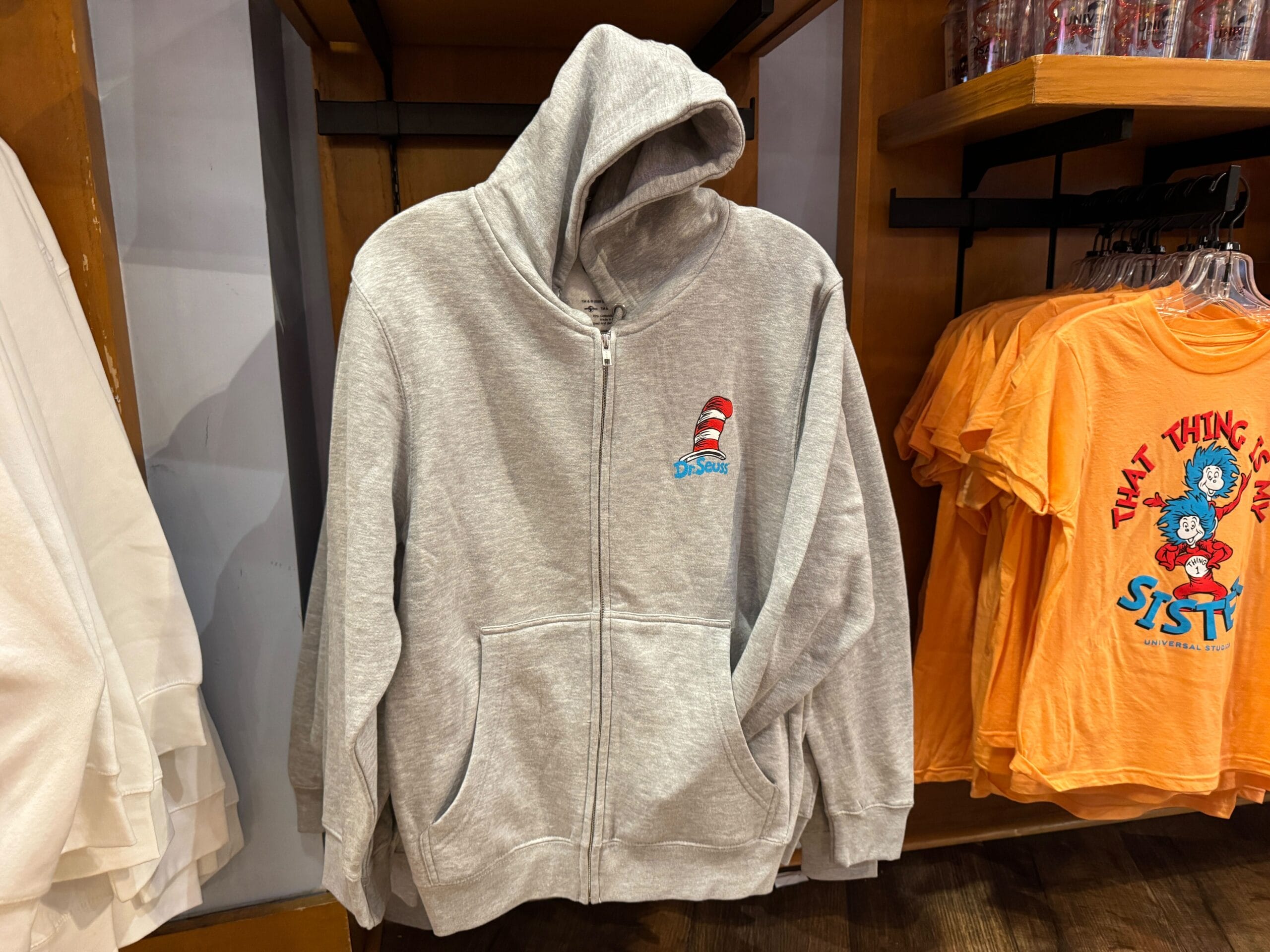 A gray zip-up hoodie with a small Cat in the Hat logo hangs among Dr. Seuss apparel at Universal, not Disney like castle gift shops.