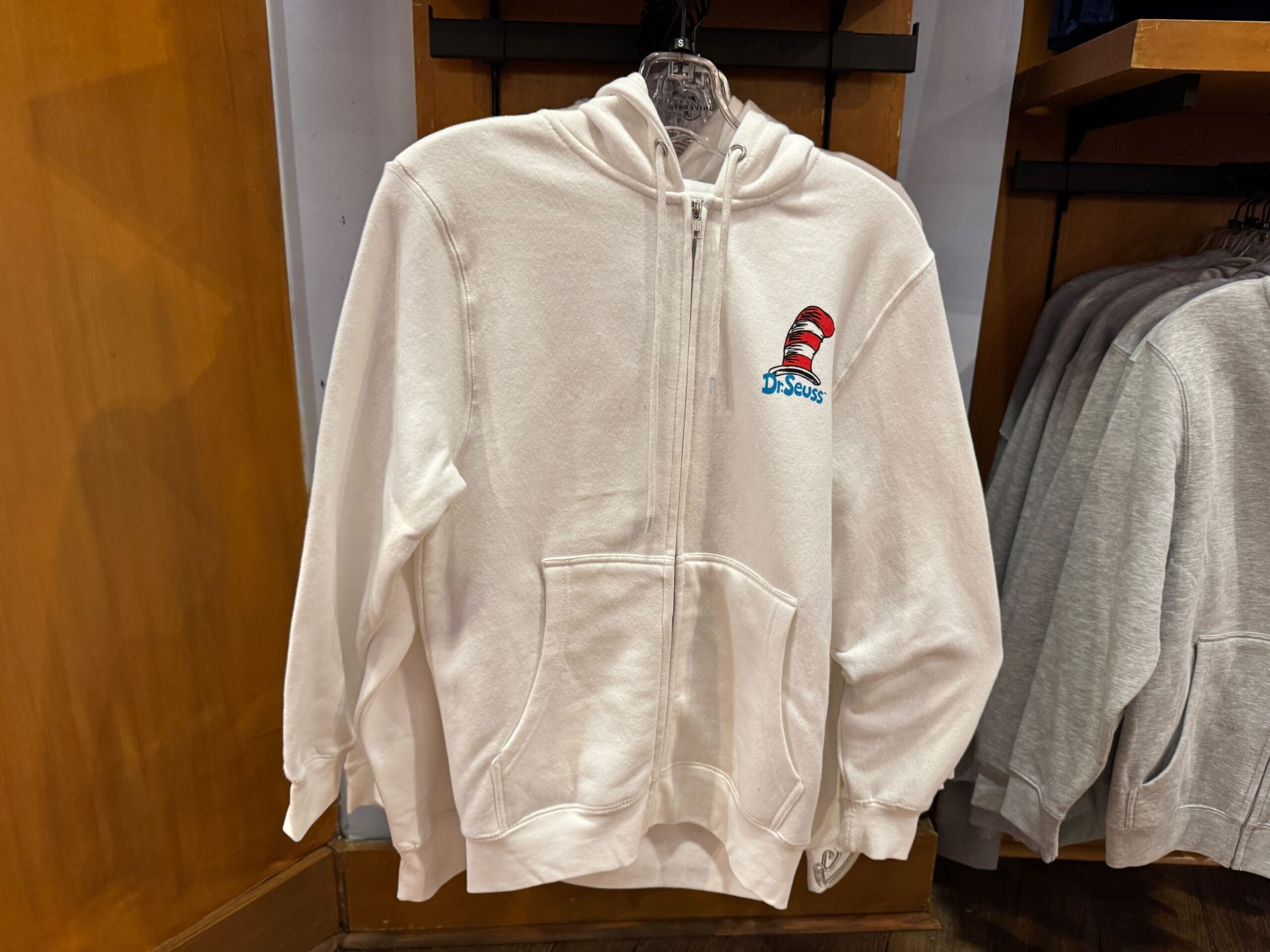 White zip-up hoodie with Dr. Seuss's red and white striped hat, a whimsical item found at Universal Studios, not Disney Parks.