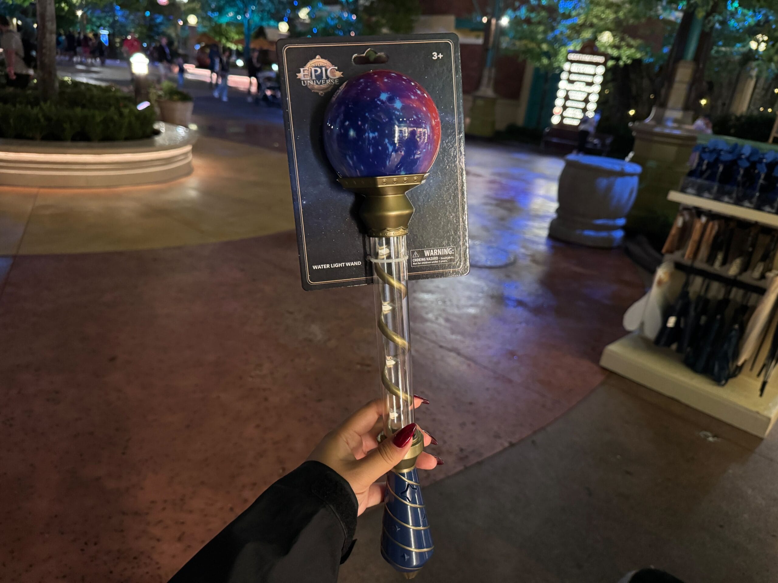 A hand holds a Celestial-Themed Water Light Wand with a glowing orb, shining bright in an epic universe at night.