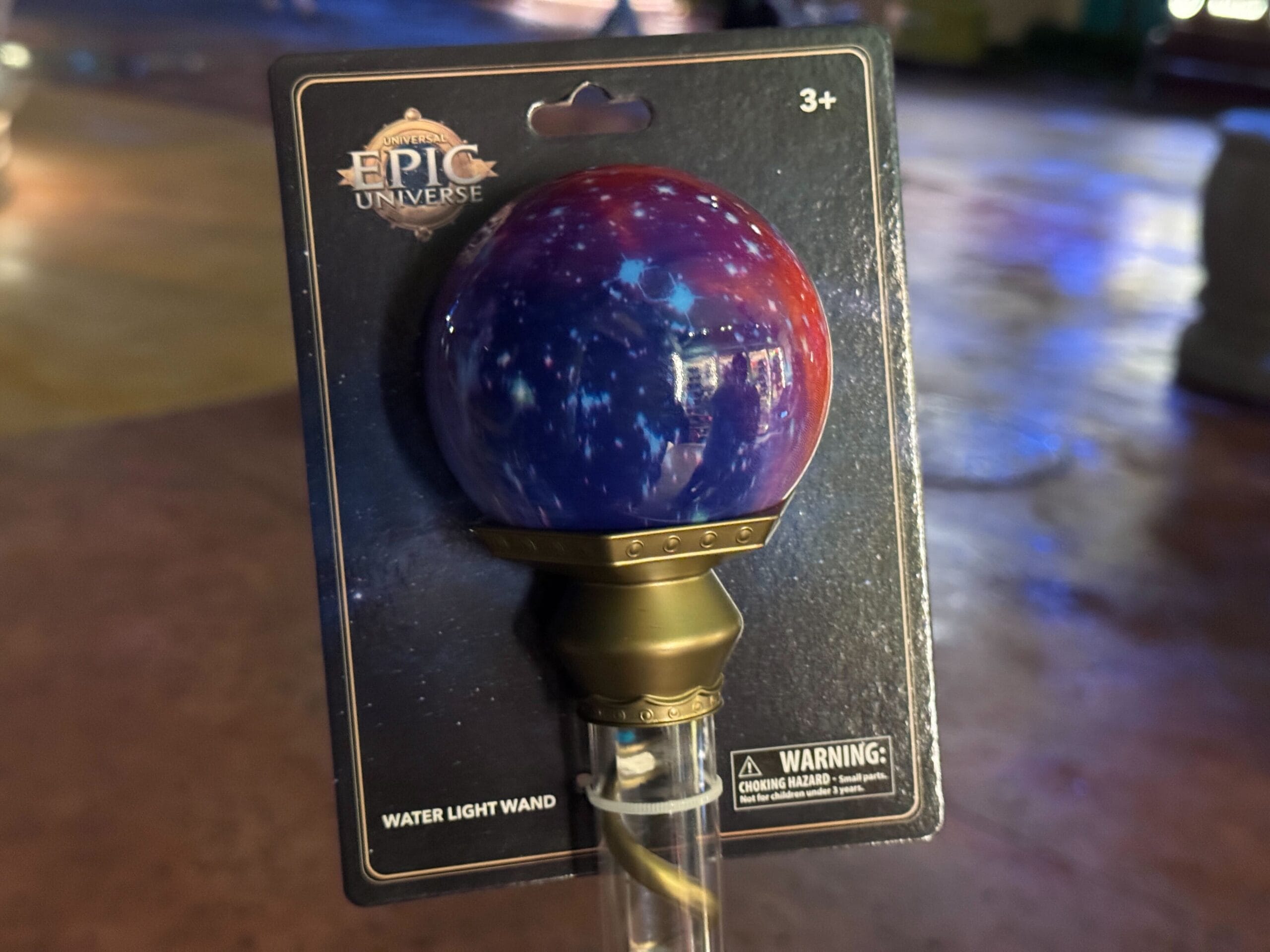 A celestial-themed water light wand from Epic Universe, featuring a galaxy globe and metallic gold base for ages 3 and up.