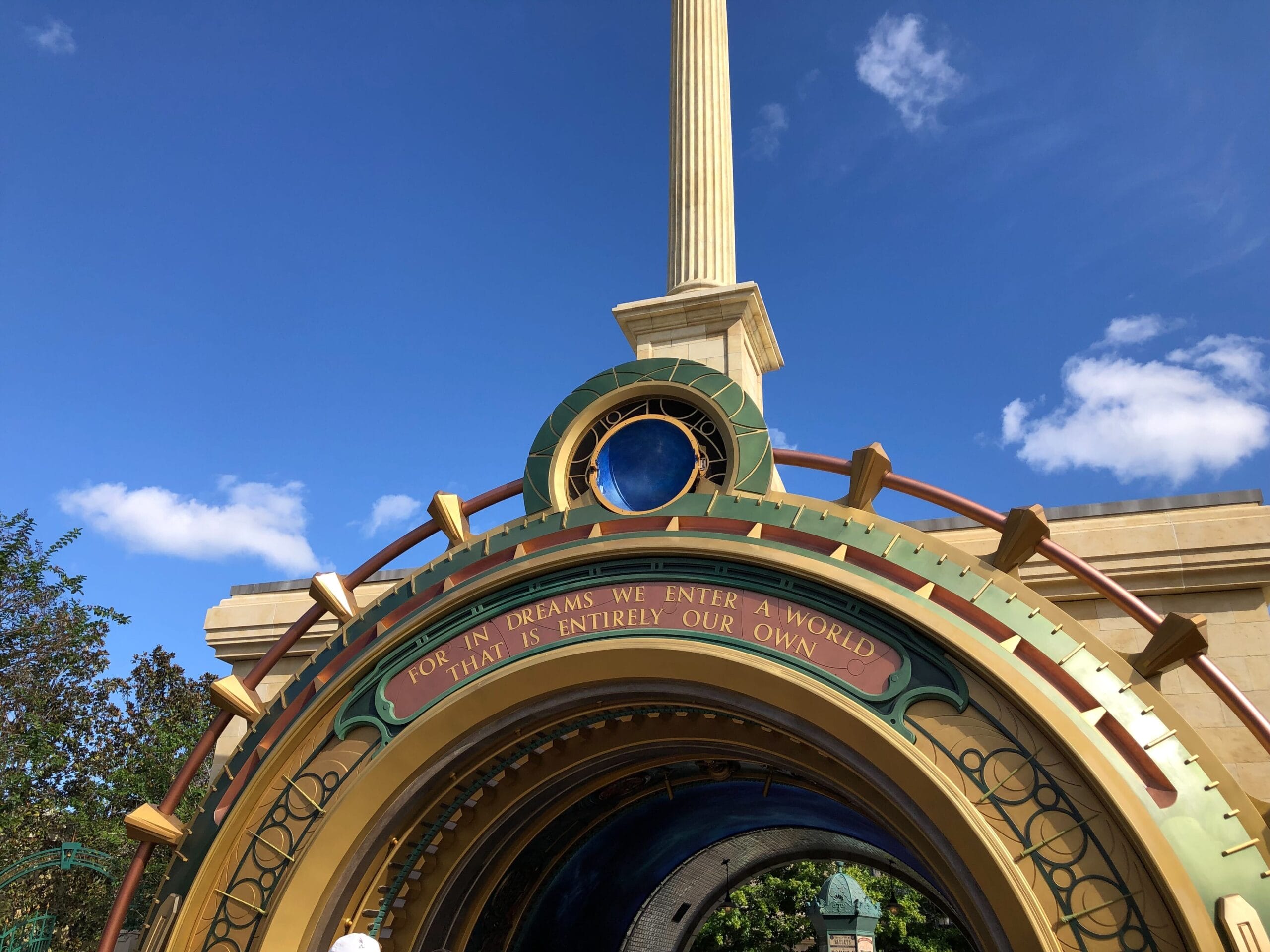 Entrance arch reminiscent of a Disney park entry, bears the quote: “For in dreams we enter a world that is entirely our own,” below bright blue skies.