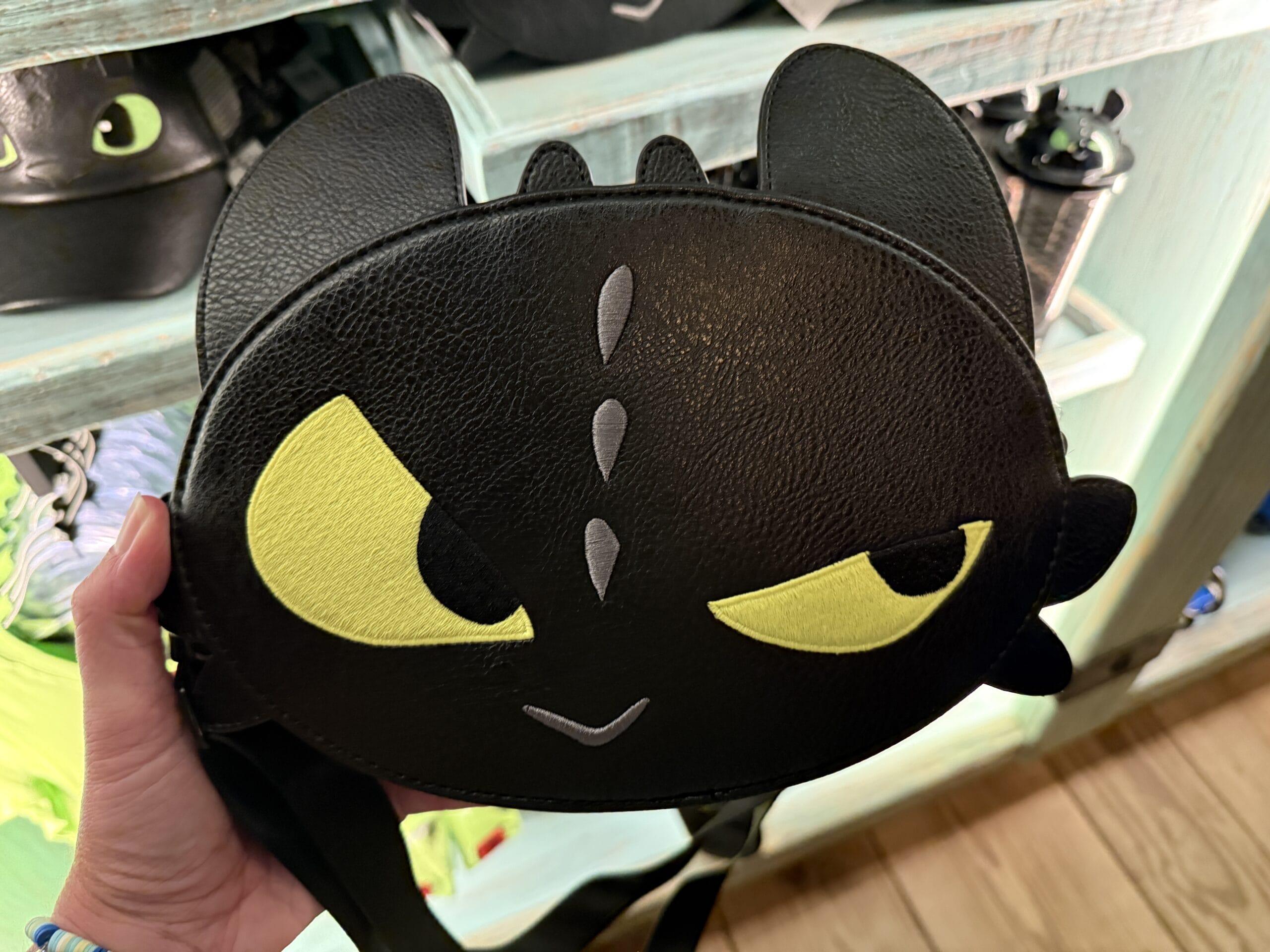 A hand holds a Toothless-shaped crossbody bag at the Spit Fyre kiosk, unique merch not found at any Disney Park castle shop.