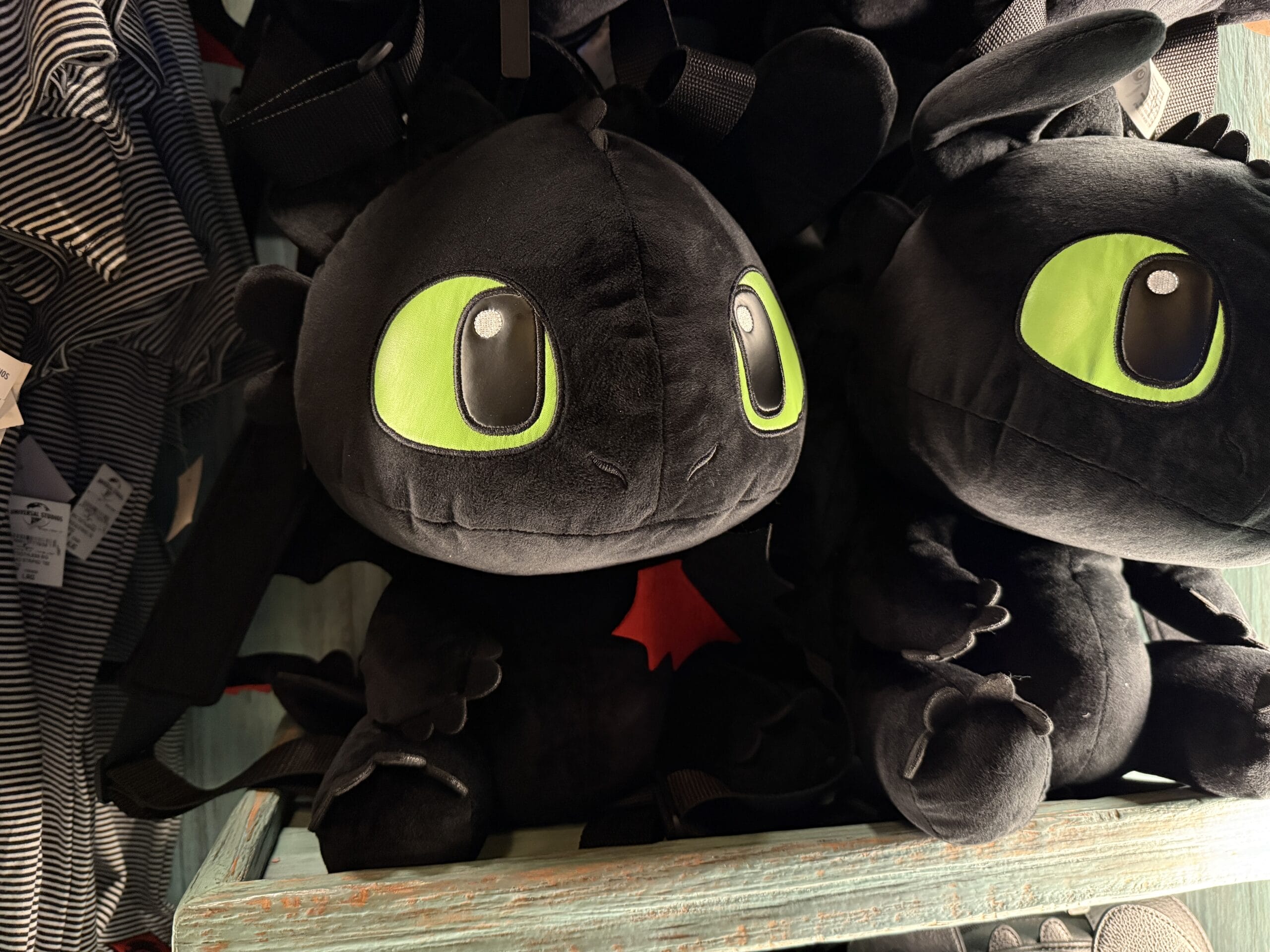 Two Spit Fyre plush dragons with big green eyes sit on a blue kiosk shelf, similar to merch found at Disney parks worldwide.