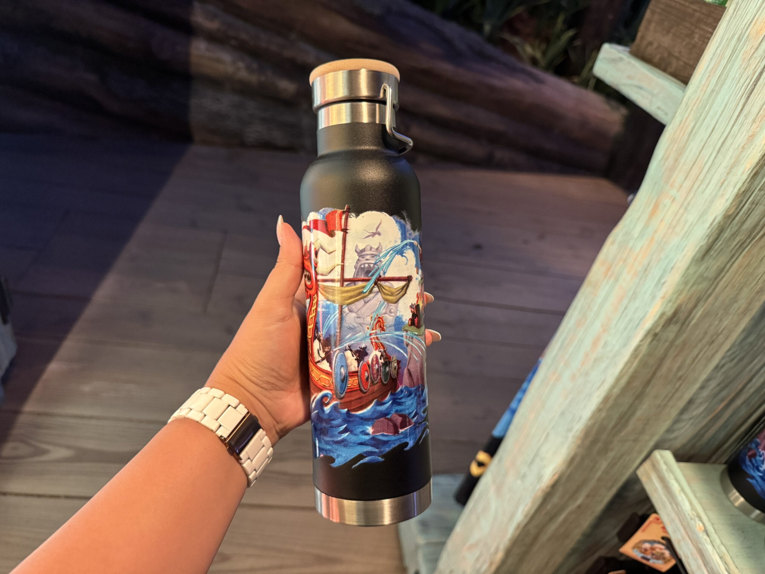 A hand holds a black water bottle featuring a vibrant pirate ship and waves, reminiscent of Disney Park ride artwork like Pirates of the Caribbean.