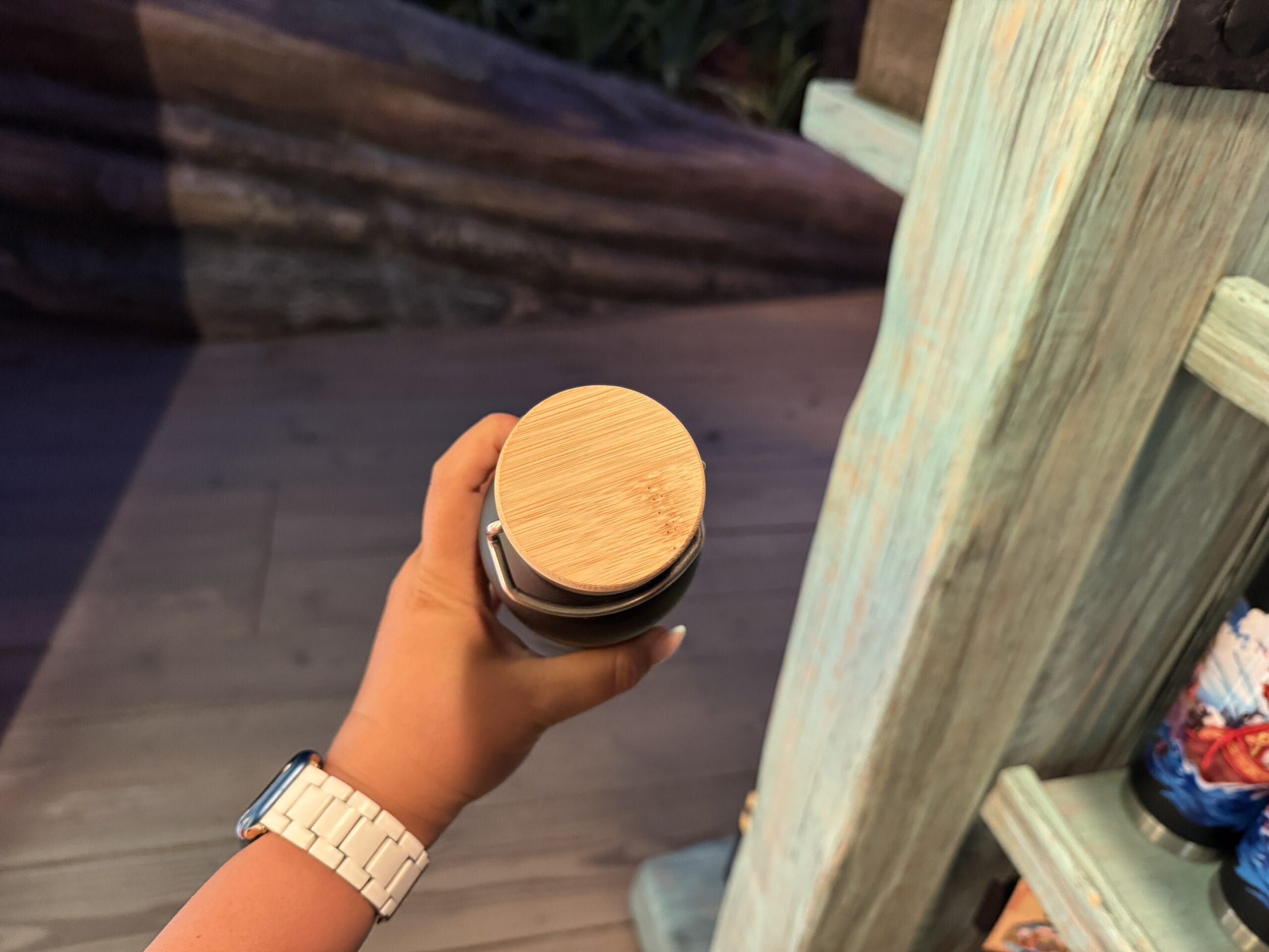 A hand with a white watch holds Spit Fyre merch—a jar with a wooden lid—by a pastel blue shelf, similar to Disney Park displays.